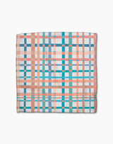 The Picnic Flowers dishcloth by Rachel Parker features a folded design with a plaid pattern in blue, turquoise, coral, and white stripes made from recycled materials, shown on a white background.
