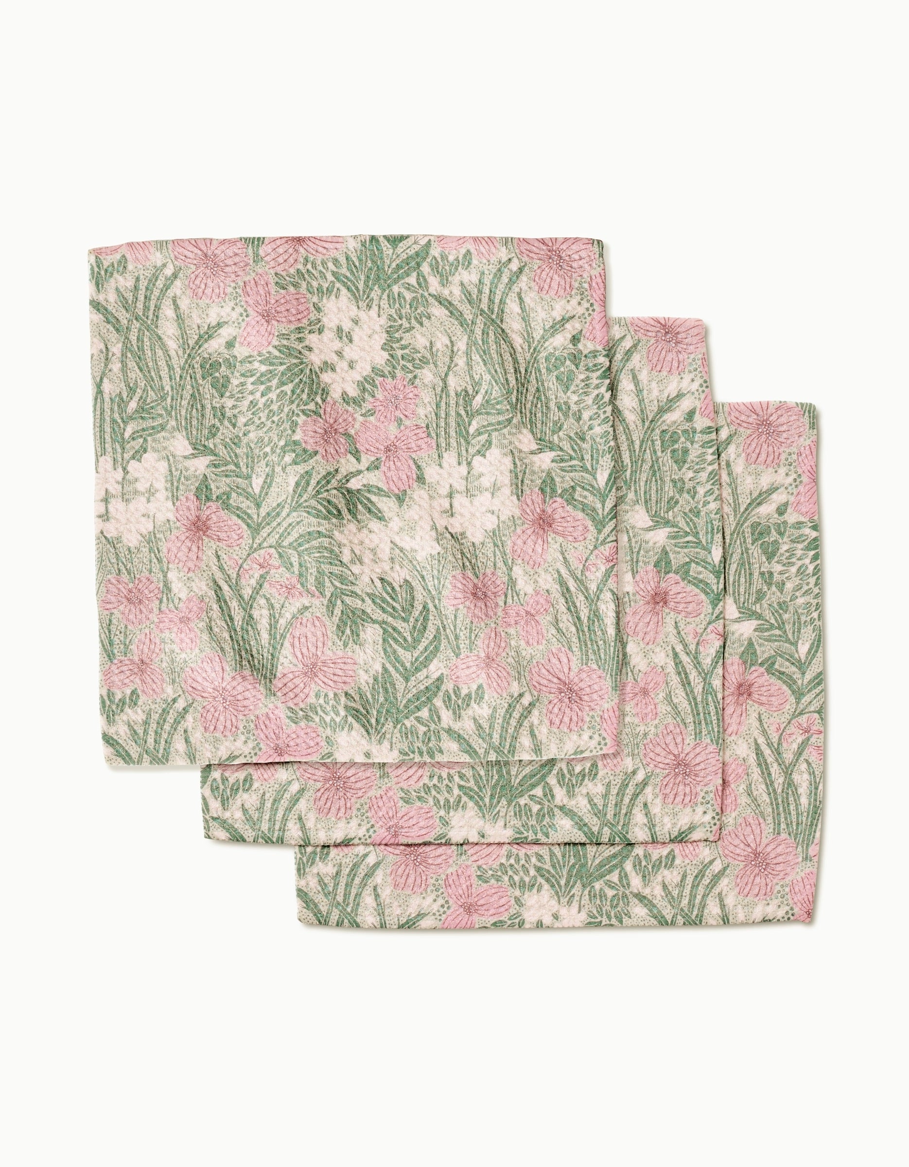 Three Pink and Sage Meadow cloth napkins by Katie OShea, made from recycled materials, feature a green and pink floral pattern with leaves on a light background and are shown stacked with slight overlap.