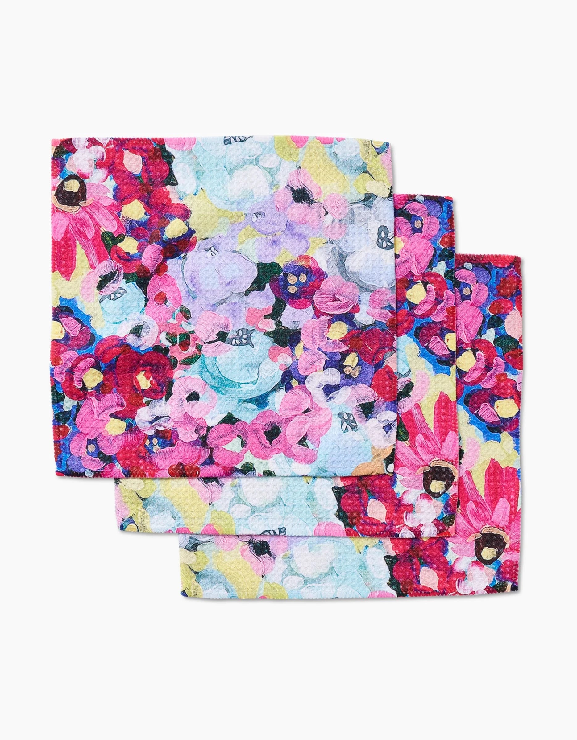 Three Pink Fields of Joy Geoweave napkins by Ania Zwara Art, featuring an abstract floral design in pink, red, purple, blue, and yellow, are layered together on a white background.