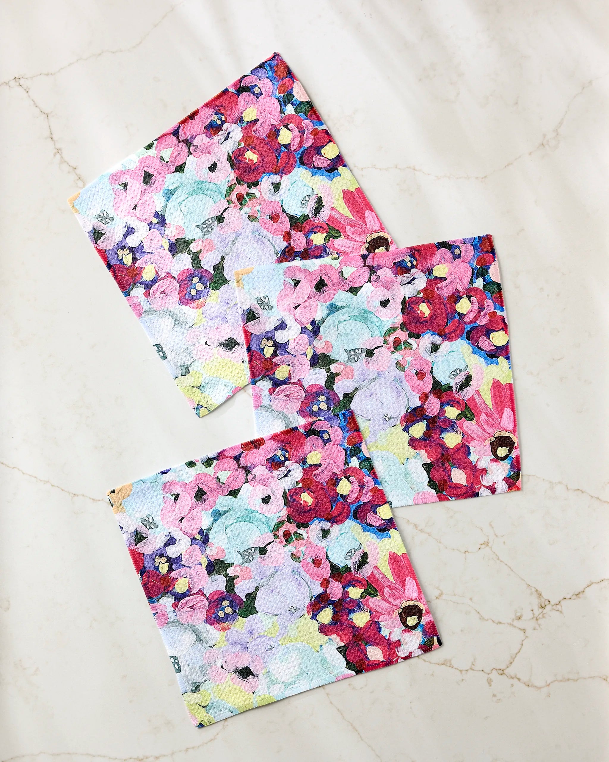 The Pink Fields of Joy dishcloth set by Ania Zwara Art features three reusable, super-absorbent towels with an abstract floral design in pink, purple, blue, and yellow—crafted from recycled materials.