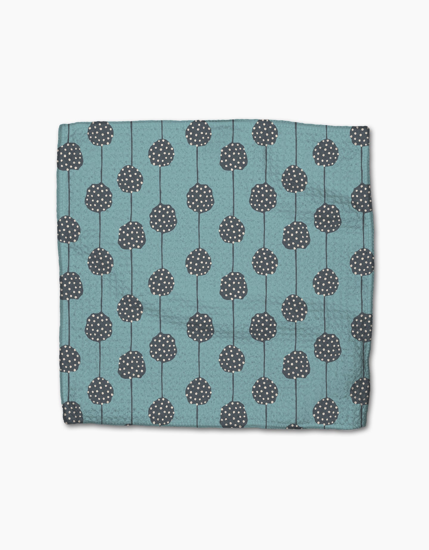 The Polka Dot Blooms napkin by Lizzie Clark is a folded teal cloth made from recycled materials, featuring dark gray circular patterns with white dots and vertical lines, displayed on a plain white background.