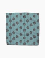 The Polka Dot Blooms napkin by Lizzie Clark is a folded teal cloth made from recycled materials, featuring dark gray circular patterns with white dots and vertical lines, displayed on a plain white background.