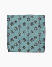 The Polka Dot Blooms napkin by Lizzie Clark is a folded teal cloth made from recycled materials, featuring dark gray circular patterns with white dots and vertical lines, displayed on a plain white background.