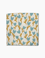 Introducing Polka Dot Blooms by Lizzie Clark—a wallet with a textured surface, adorned with blue tulip-inspired flowers and mustard stems on white, capturing the whimsical charm of super-absorbent recycled dishcloths.