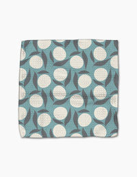 The Polka Dot Blooms quilted dishcloth set by Lizzie Clark is made from recycled materials and features a blue background with white circles and overlapping gray leaves.