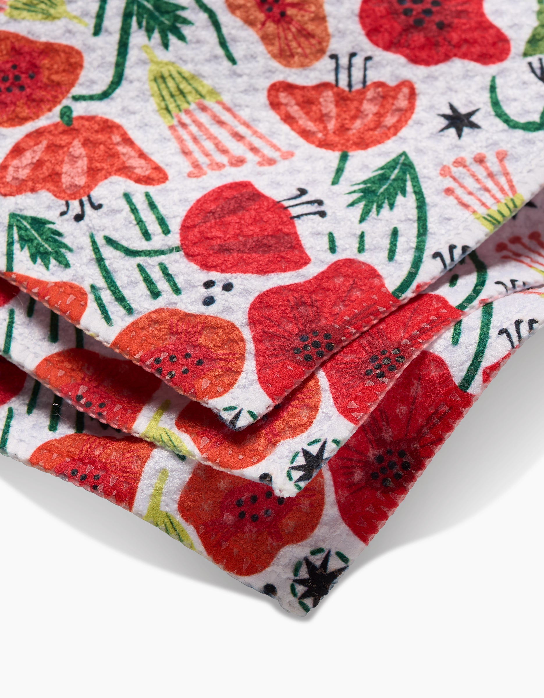 Close-up of Elisabeth Wing’s Poppy Power Geoweave fabric, showcasing vibrant red poppies with green stems and leaves on white. The folded layers highlight its versatile use as a dishcloth or for other household needs.