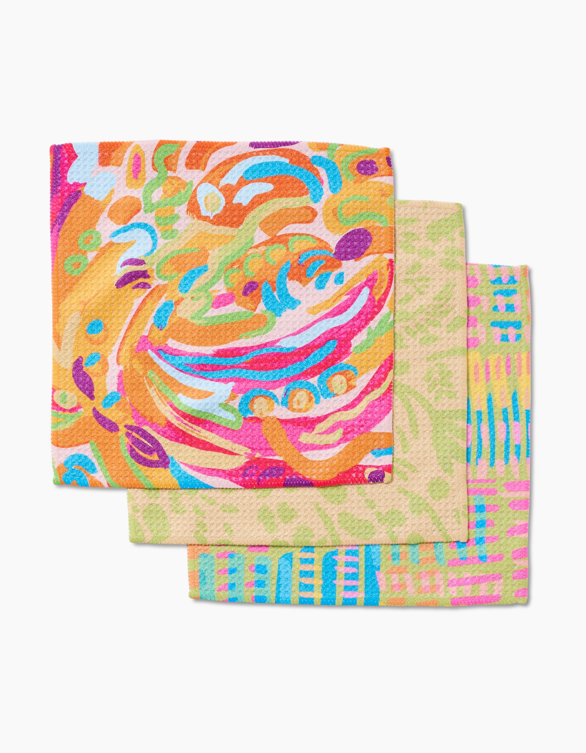 Three vibrant square napkins from Sareka Unique’s Positive Vibes set are stacked: the top shows swirling abstracts, the middle has green leaves on beige, and the bottom displays blue, pink, and yellow geometric lines. All are made from recycled materials.