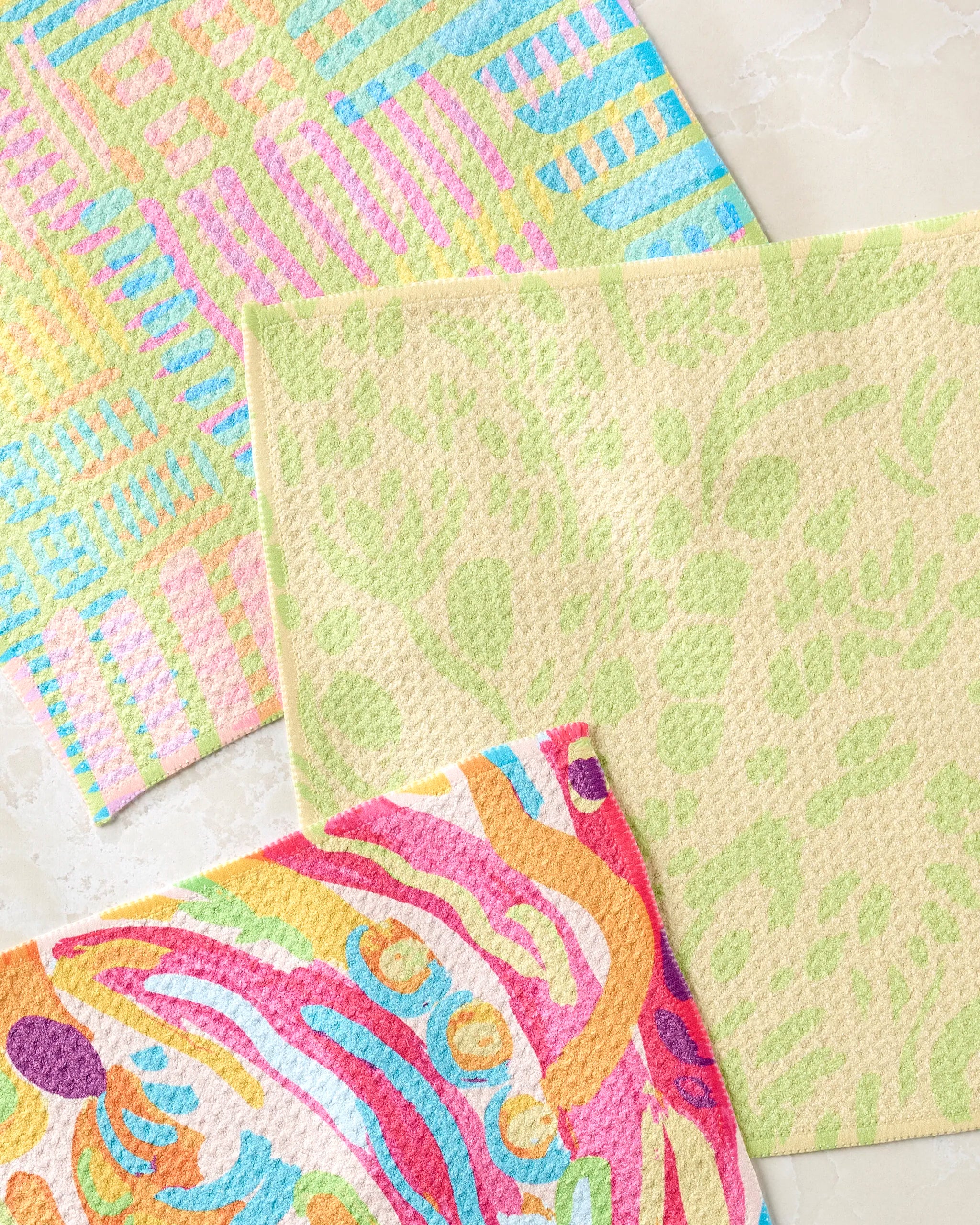 The Sareka Unique Positive Vibes set includes three super-absorbent, eco-friendly sponge cloths in pastel geometric patterns, light green abstract designs, and bold multicolored swirls on a beige background.