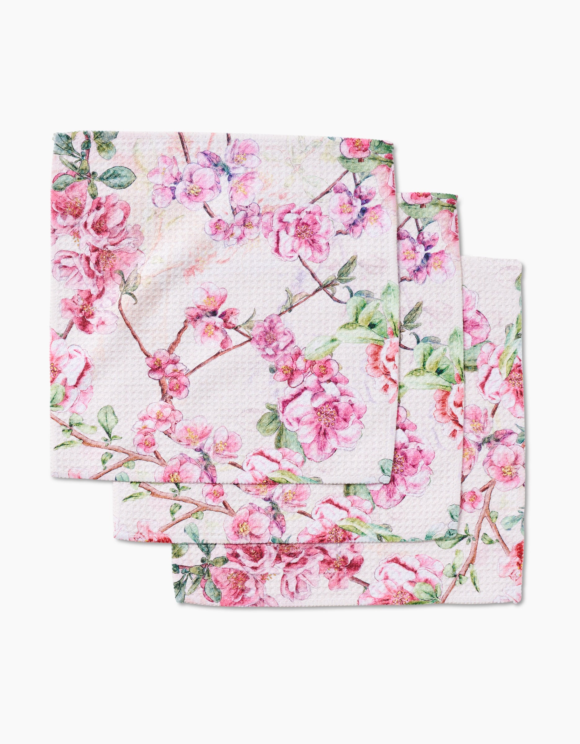 Three folded Primroses cloth napkins by Pascale Dilger, made from Geoweave fabric with a pink and green blooming floral print, are stacked neatly on a white background.