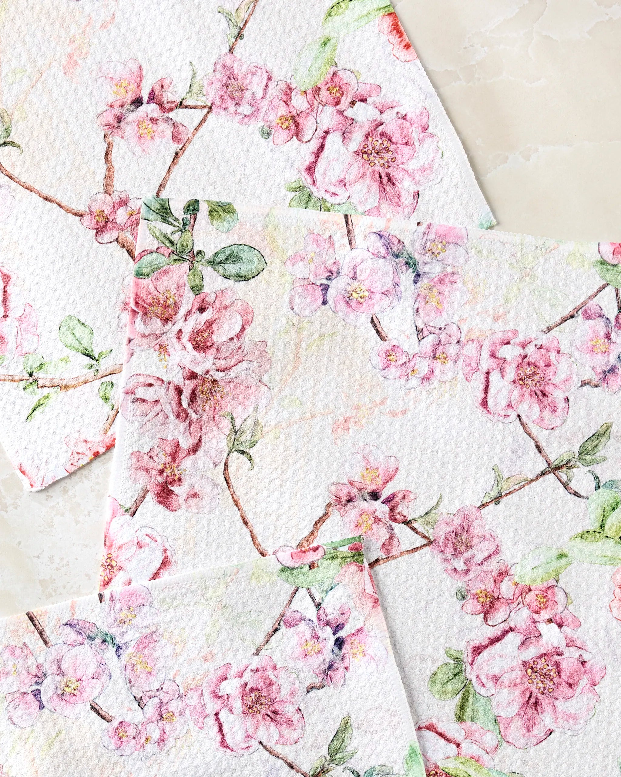 Three "Primroses" paper napkins by Pascale Dilger feature a textured surface with watercolor-style pink primroses and green leaves on a light marble background—perfect to complement your favorite absorbent kitchen towels.