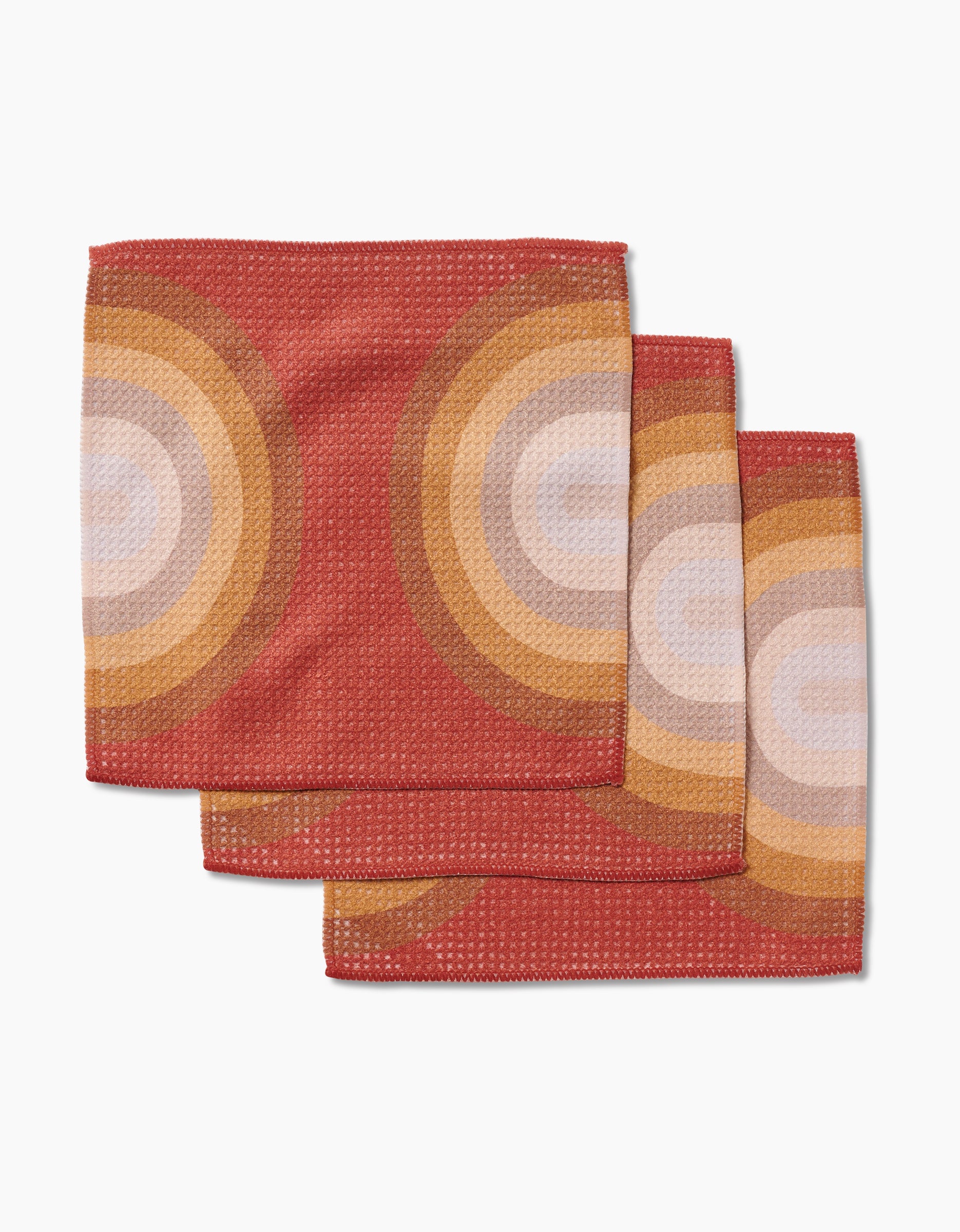 Three GEOMETRY Pumpkin Spice dishcloths, featuring a retro concentric circle pattern in tan, orange, and cream, are stacked on a white background. Made from Geoweave fabric for top absorbency and quick drying.