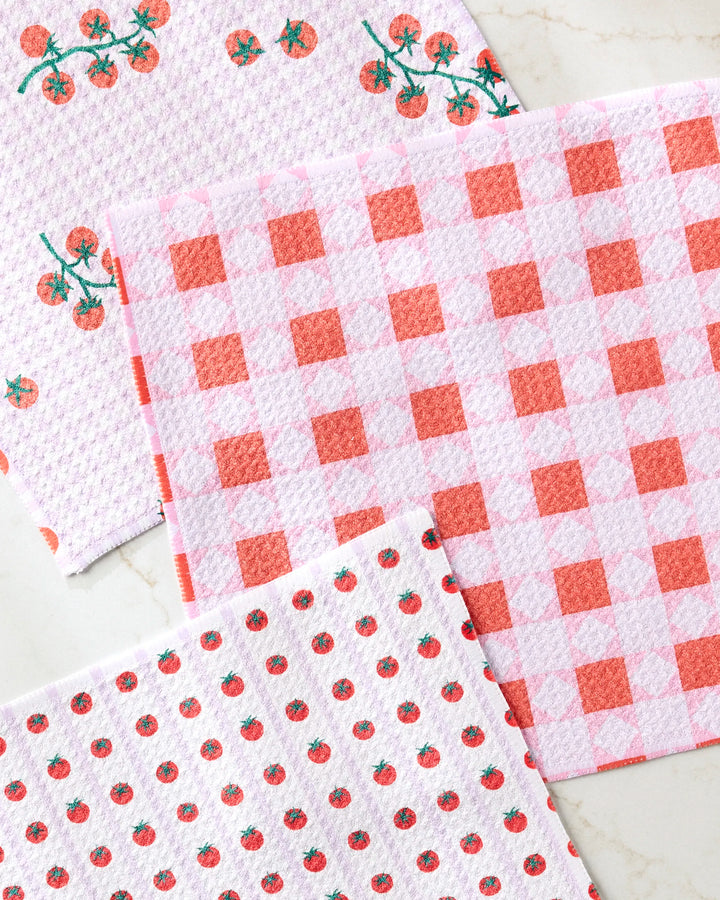 Three super-absorbent Brittany Jepsen Quilt Tomato Harvest dishtowels, featuring tomato prints, red and white checks, and embroidered tomato vines, are displayed on a marble surface.