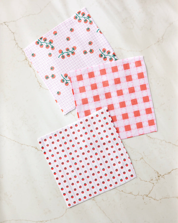 Three "Quilt Tomato Harvest" dishcloths by Brittany Jepsen, crafted from recycled materials, are displayed on marble. Featuring floral, gingham check, and polka dot patterns, this eco-friendly set adds charm to any kitchen.