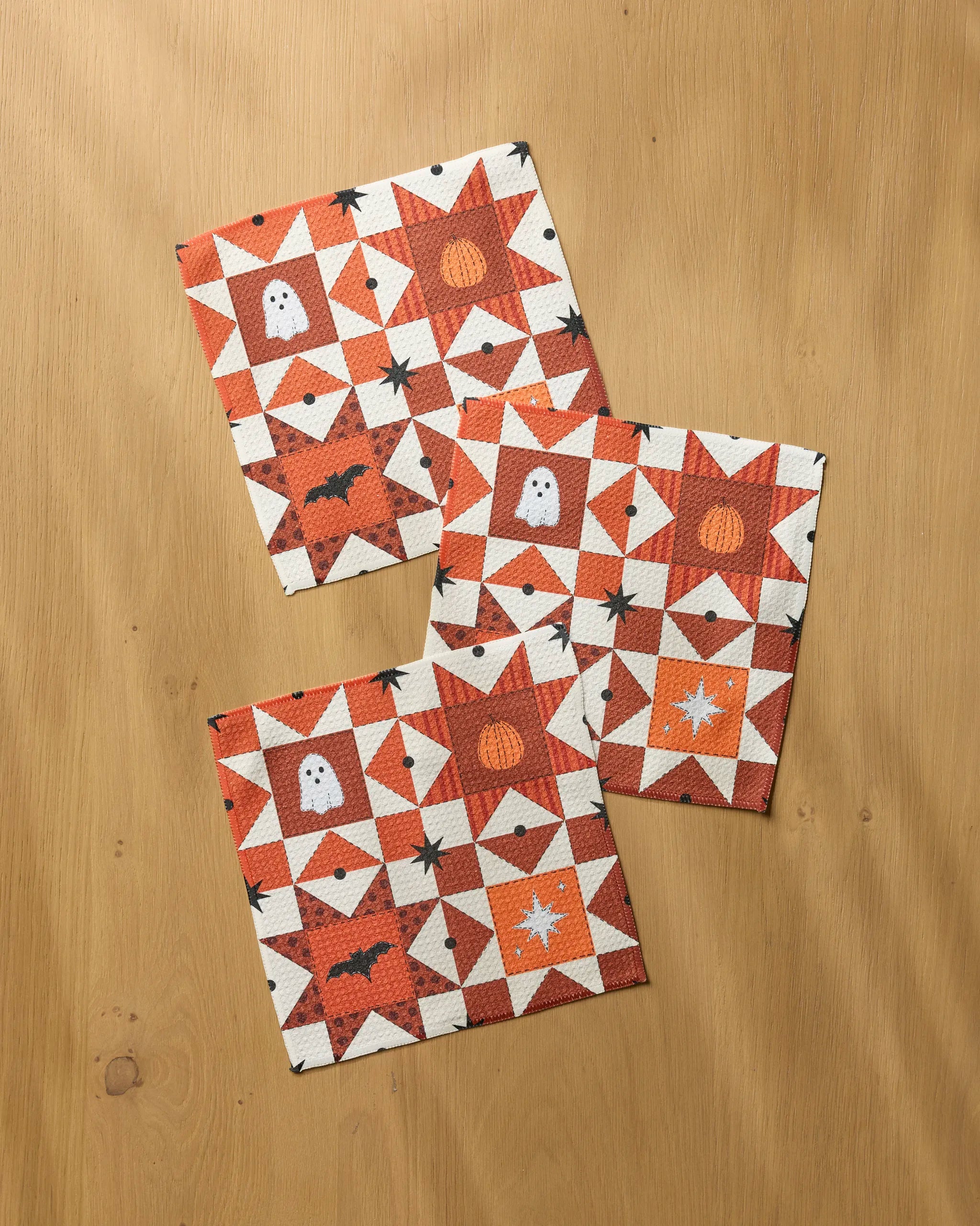The Geometry Quilt Work set includes three quilted square coasters made from recycled materials, featuring festive Halloween patterns in orange, white, and black for a charming seasonal touch.