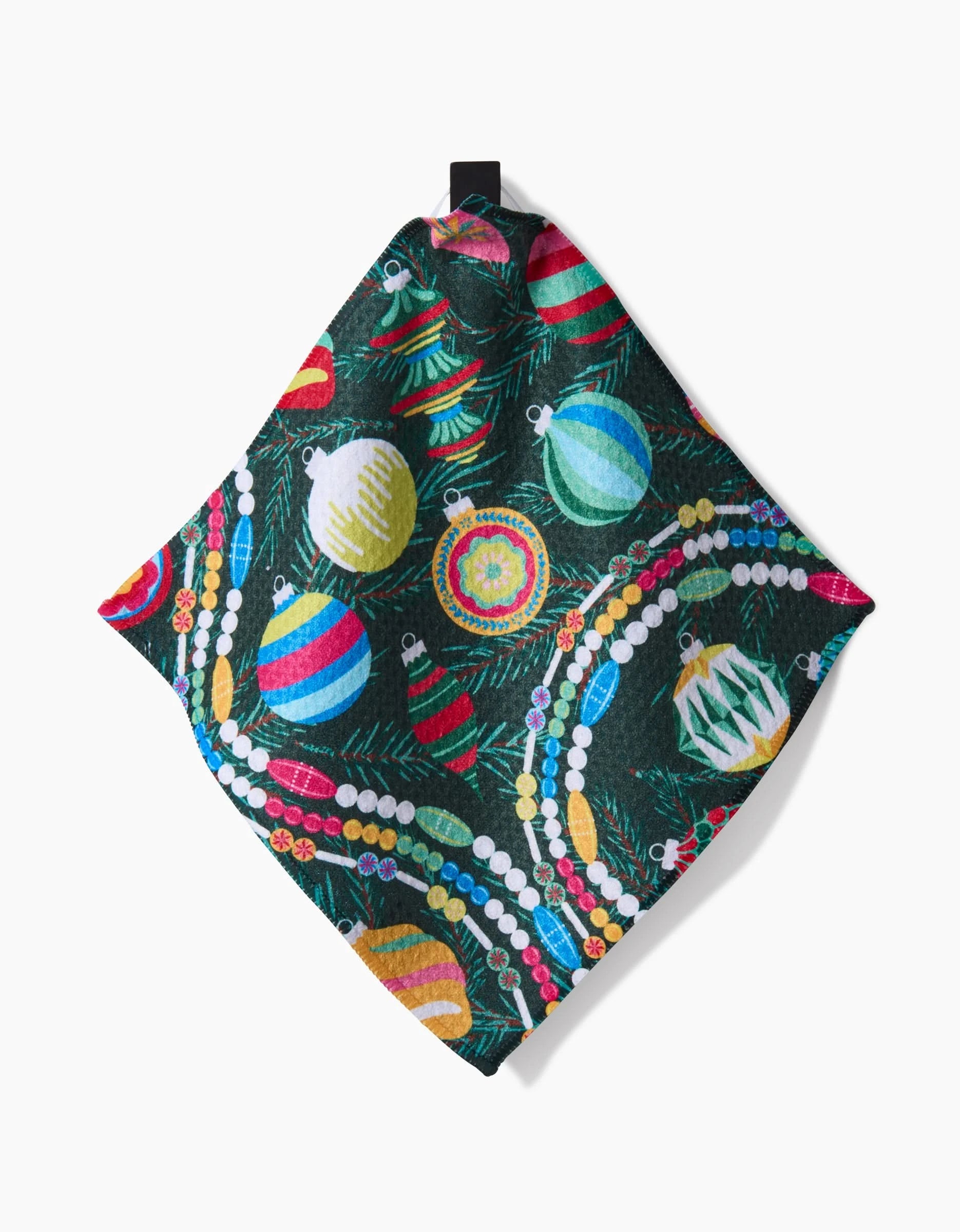 The Retro Holly napkin by Rebecca Bobko is a square Geoweave fabric piece featuring Christmas ornaments and garlands on a dark green background, folded with a black tag at the top.