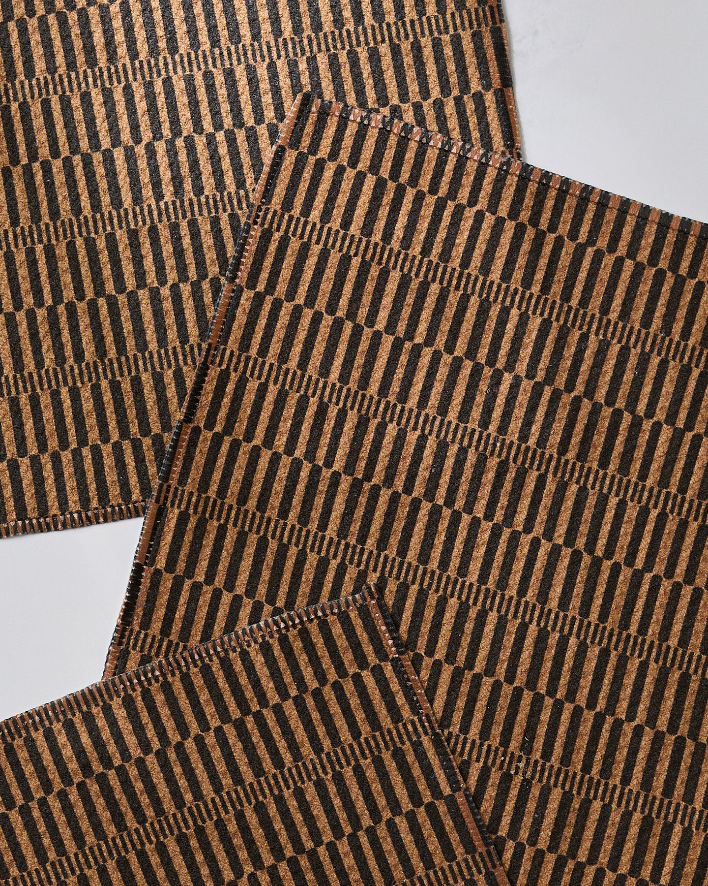 Four Ridge cork placemats by Geometry, featuring a repeating black geometric vertical line pattern, arranged overlapping on a white surface. Made from recycled materials for an eco-friendly touch.
