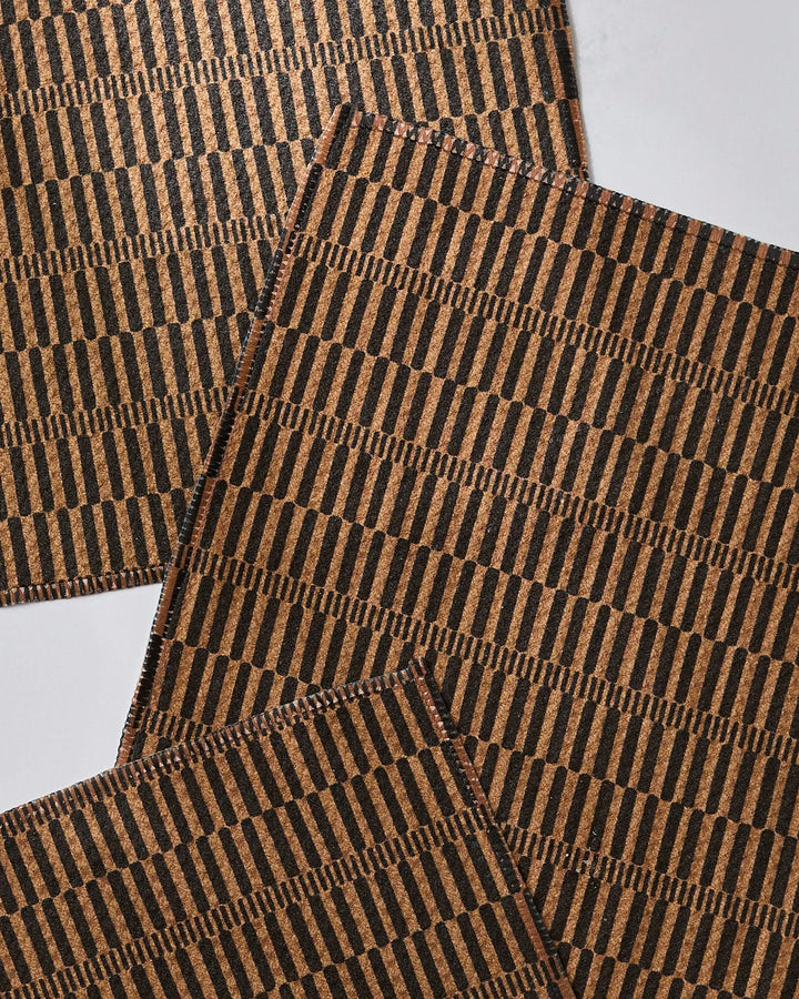 Four Ridge cork placemats by Geometry, featuring a repeating black geometric vertical line pattern, arranged overlapping on a white surface. Made from recycled materials for an eco-friendly touch.