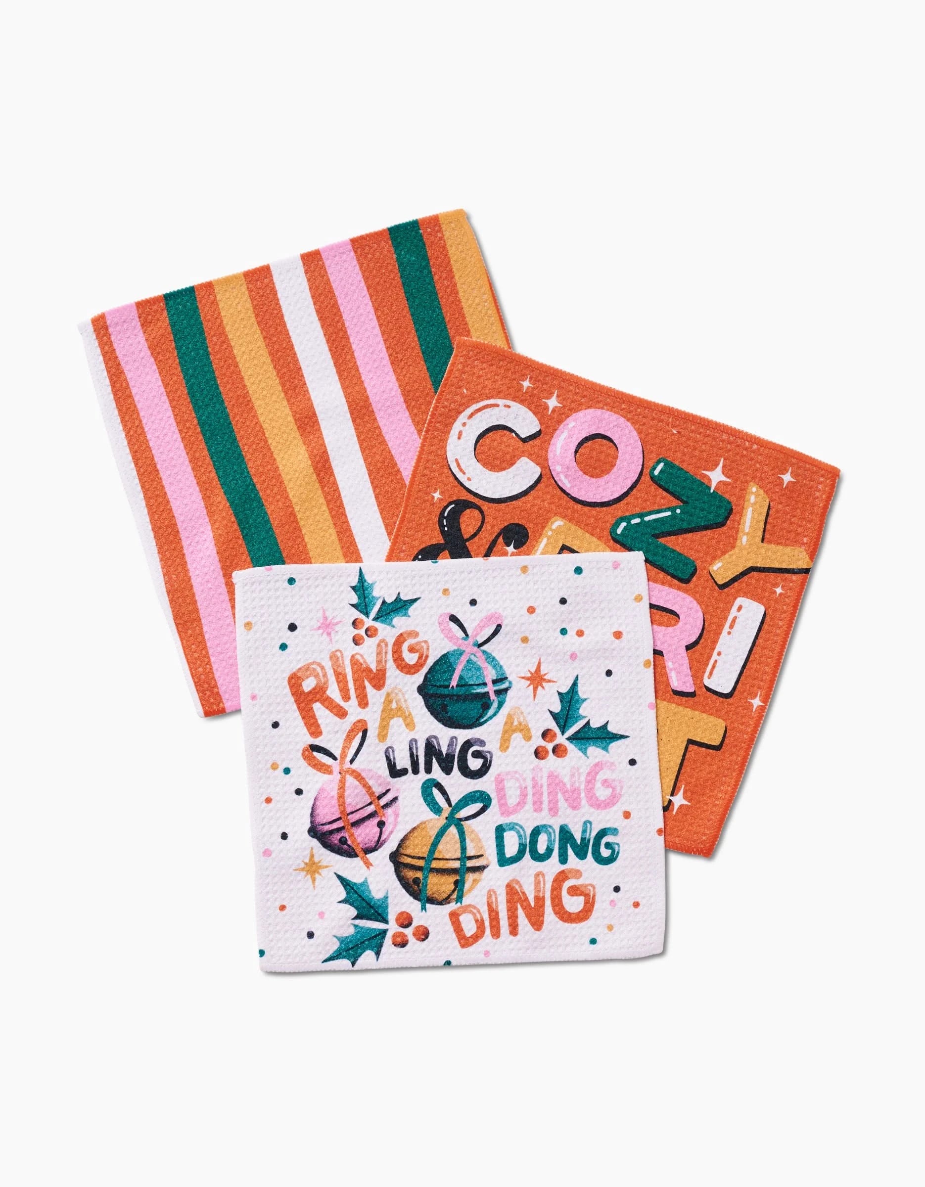 The Megan Roy Ring-A-Ling set includes three recycled holiday napkins: one striped in pink, orange, red, and green; one with COZY & MERRY in bold; and one with holly leaves plus RING A LING DING DONG DING.