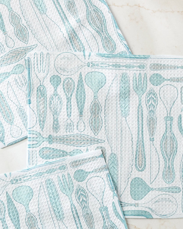 Three white Romy Wares dishcloths by Amy MacCready, featuring a light blue cutlery pattern, are arranged on marble—an eco-friendly recycled set perfect for any kitchen.