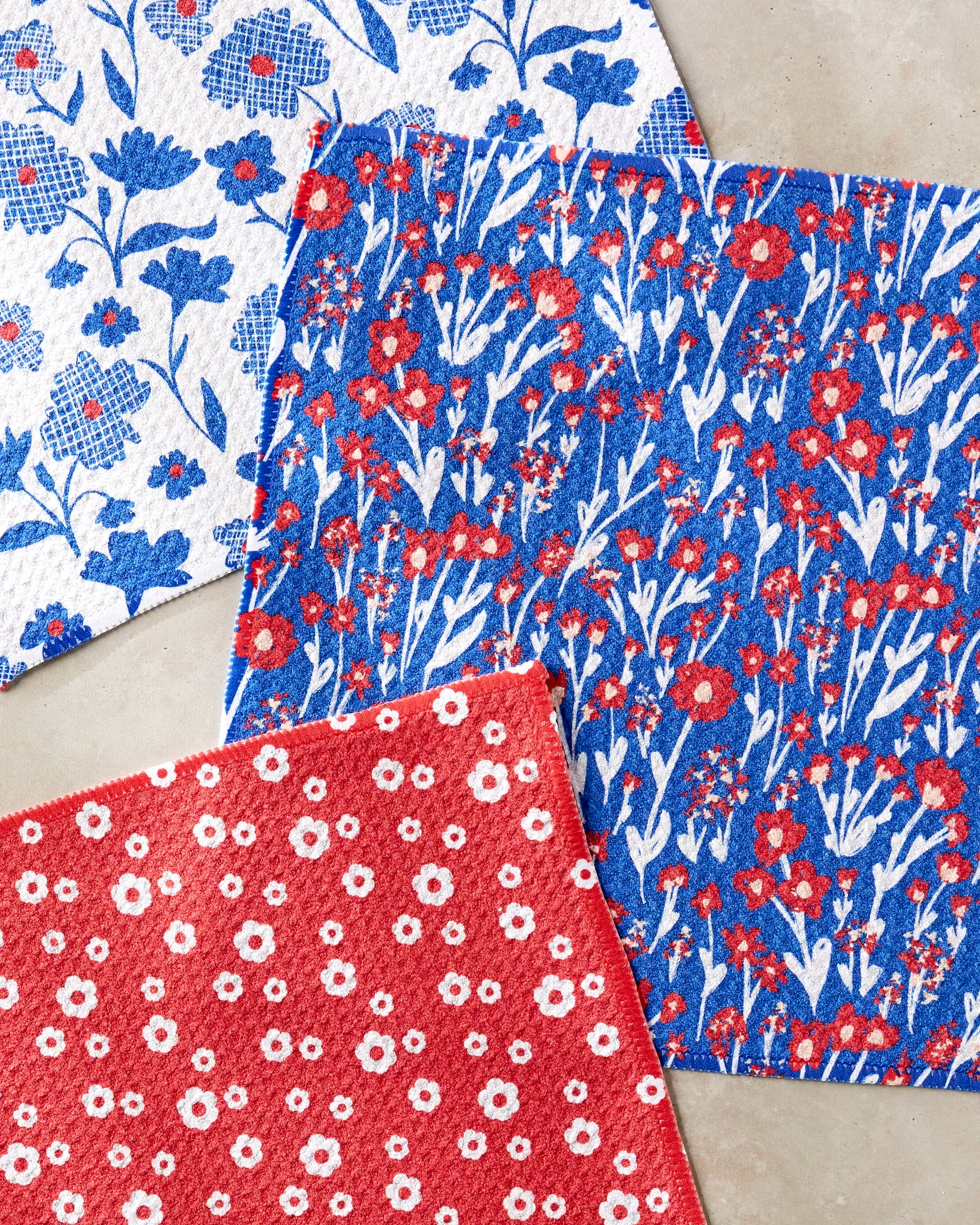 The Danelys Sidron "Royal Garden" set features three square dishcloths made from recycled materials, each with floral patterns: red with white flowers, blue with red and white, and white with blue and red.