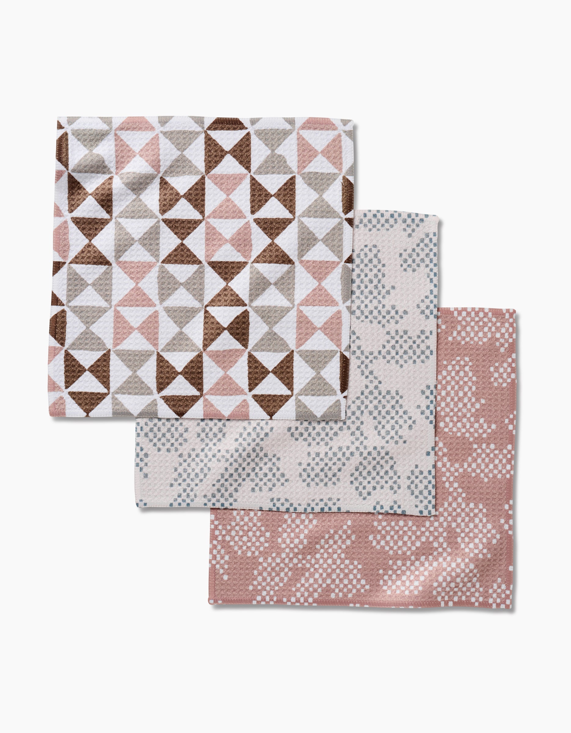 Three folded Studio Jeannot Rubix Pixie dishcloths with geometric patterns in brown, pink, and white Geoweave fabric, overlapping on a white background.