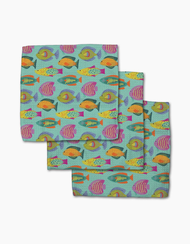 The Geometry Schooling set includes three cloth napkins featuring a colorful fish pattern on light teal, made from post-consumer recycled materials—an eco-friendly and cheerful addition to your table.