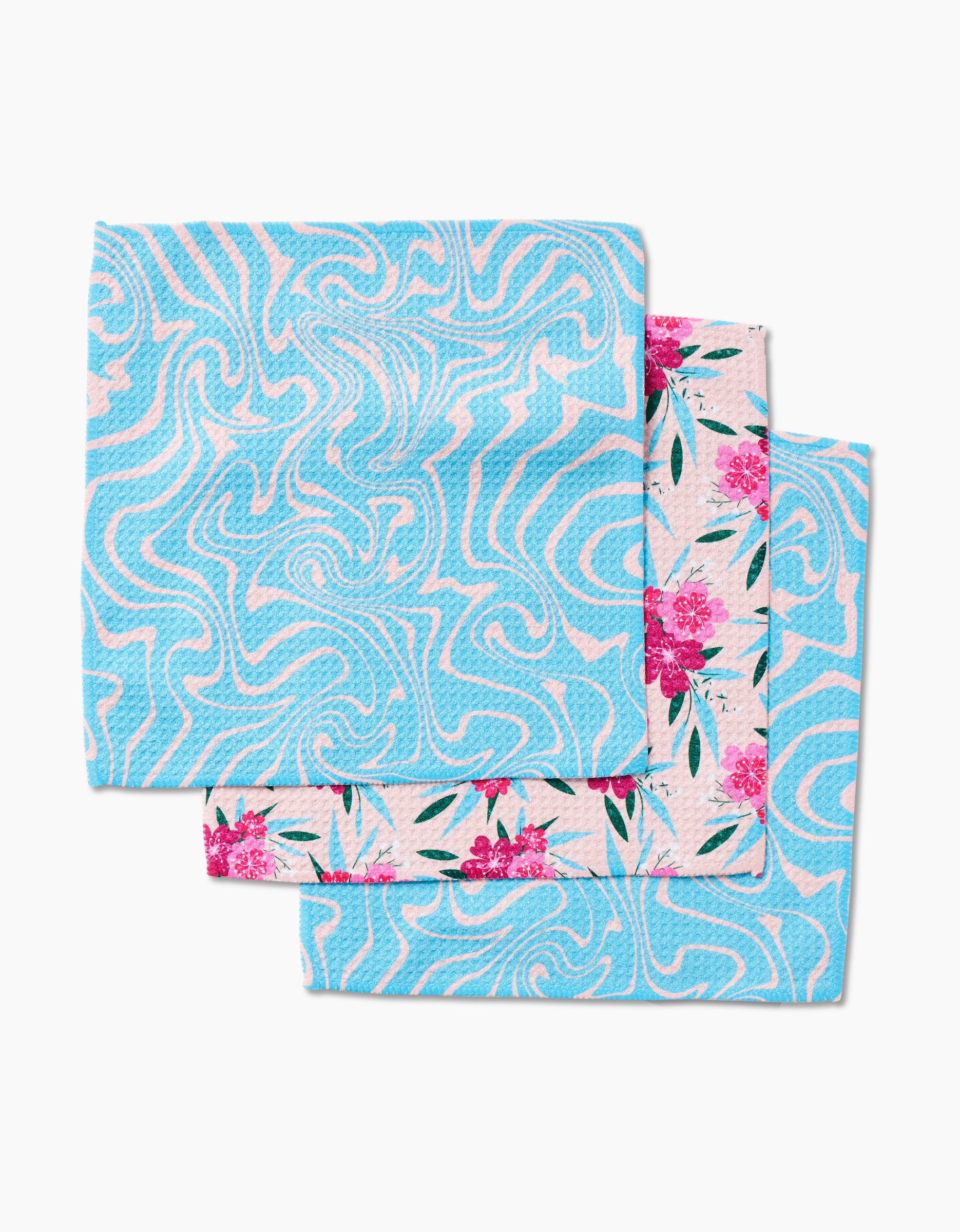 Two folded cloths stacked; the top is blue with a wavy white swirl pattern, while the bottom partially shows a floral design—GEOMETRY’s Sending Love super-absorbent dishcloth set adds style and function to your kitchen.