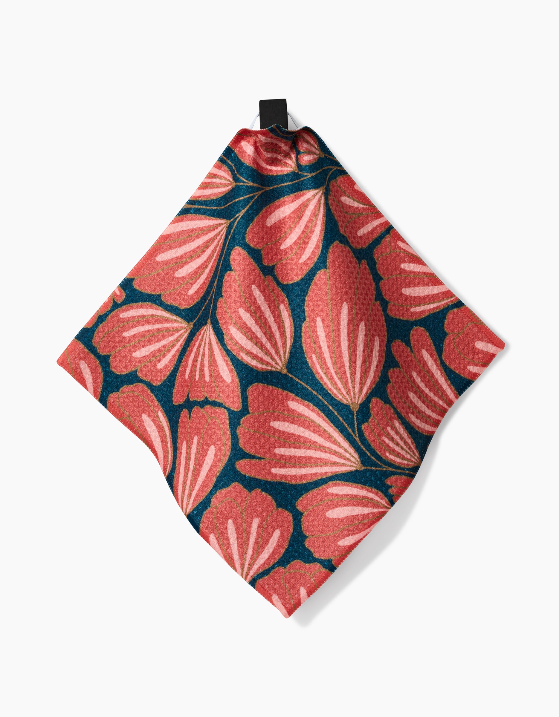 The Sheila Flower cloth napkin by Amy MacCready features pink and coral stylized leaves on dark teal Geoweave fabric, displayed hanging by a black loop against a white background.