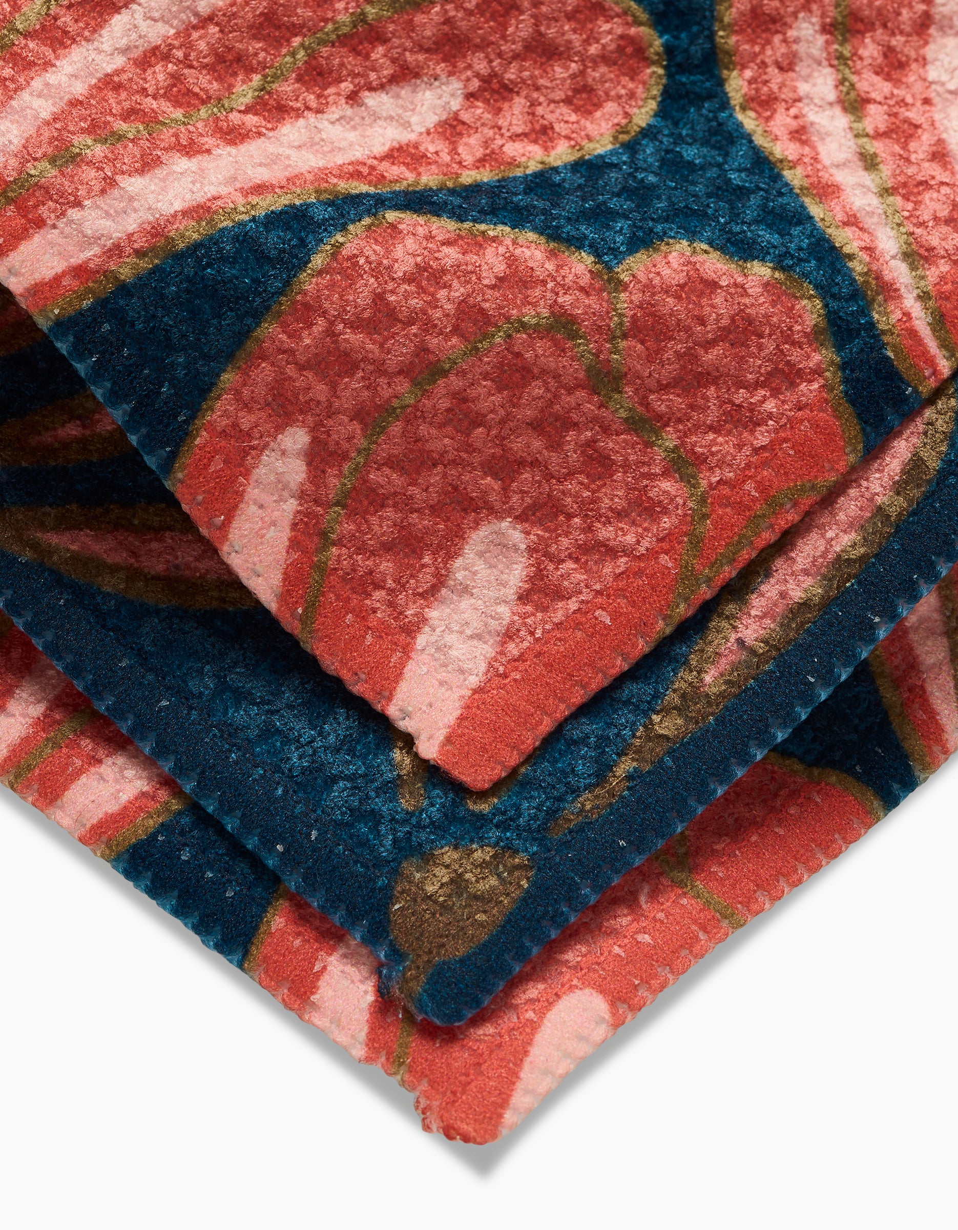 A close-up of the Sheila Flower Geoweave dishcloth by Amy MacCready, featuring a red and pink floral pattern on a dark blue background. The soft, textured fabric has visible edge stitching.
