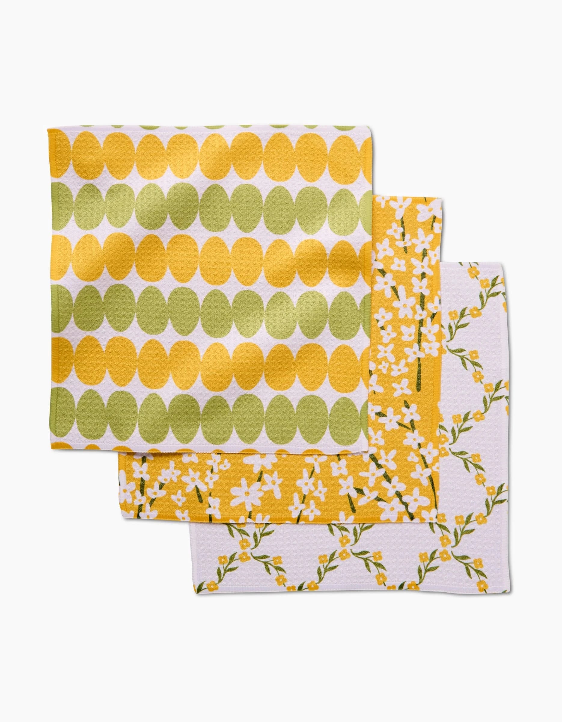 The Kayla Ann Signs of Springtime set includes three Geoweave cloth napkins: one with yellow and green ovals, one with small white flowers and yellow accents, and one with yellow and green floral branches on white.