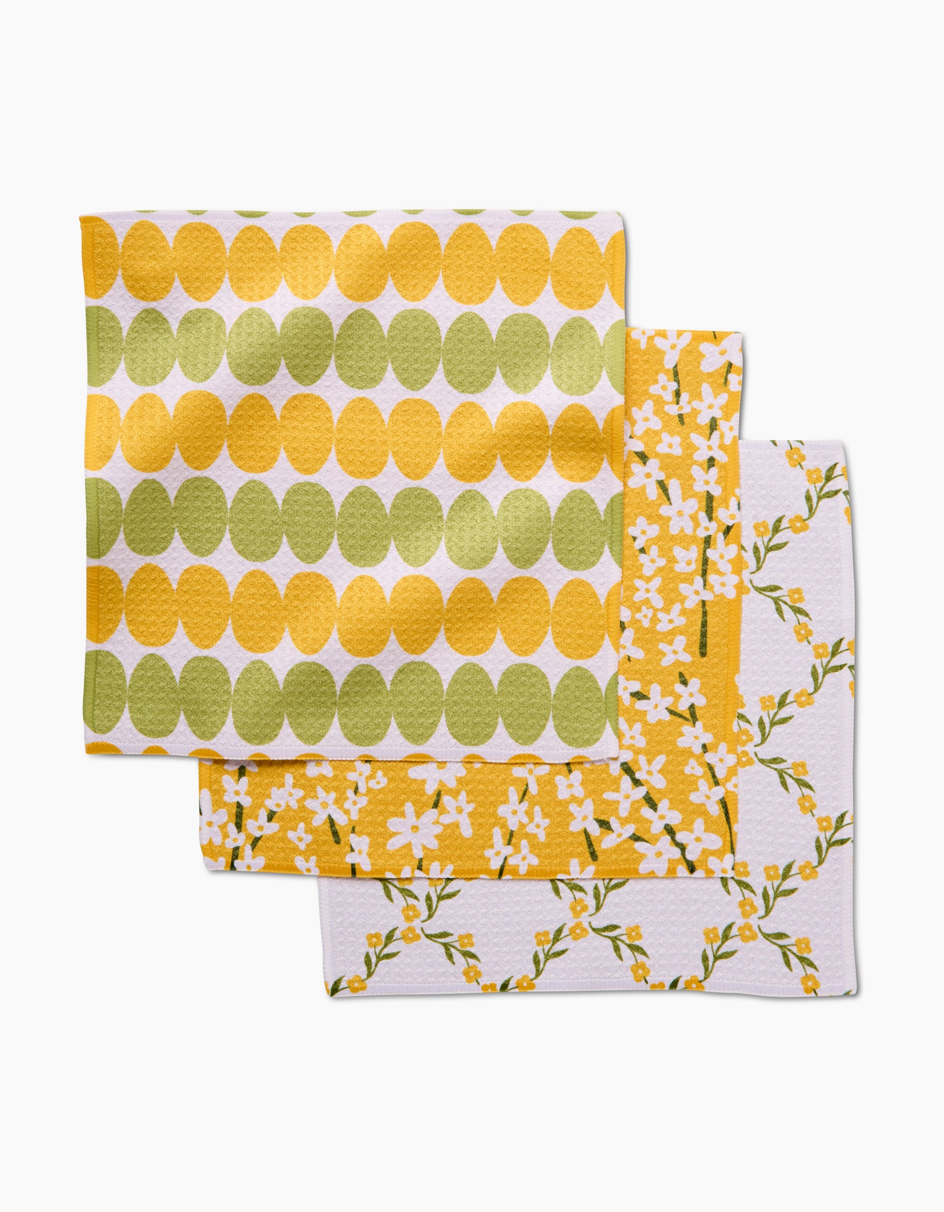 The Kayla Ann Signs of Springtime set includes three Geoweave cloth napkins: one with yellow and green ovals, one with small white flowers and yellow accents, and one with yellow and green floral branches on white.