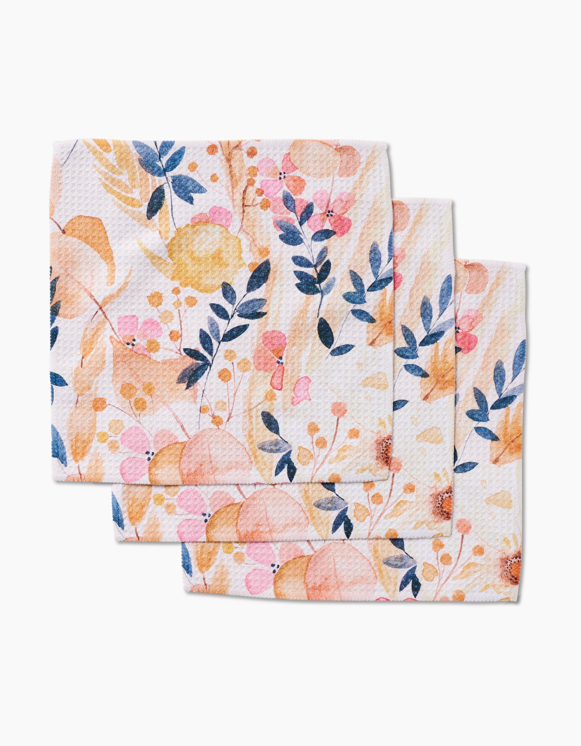 Three Sleepy Fields paper napkins by GEOMETRY, featuring a watercolor floral design in orange, pink, and blue with leaves and berries. Inspired by dishcloths, they are stacked neatly and slightly overlapping.