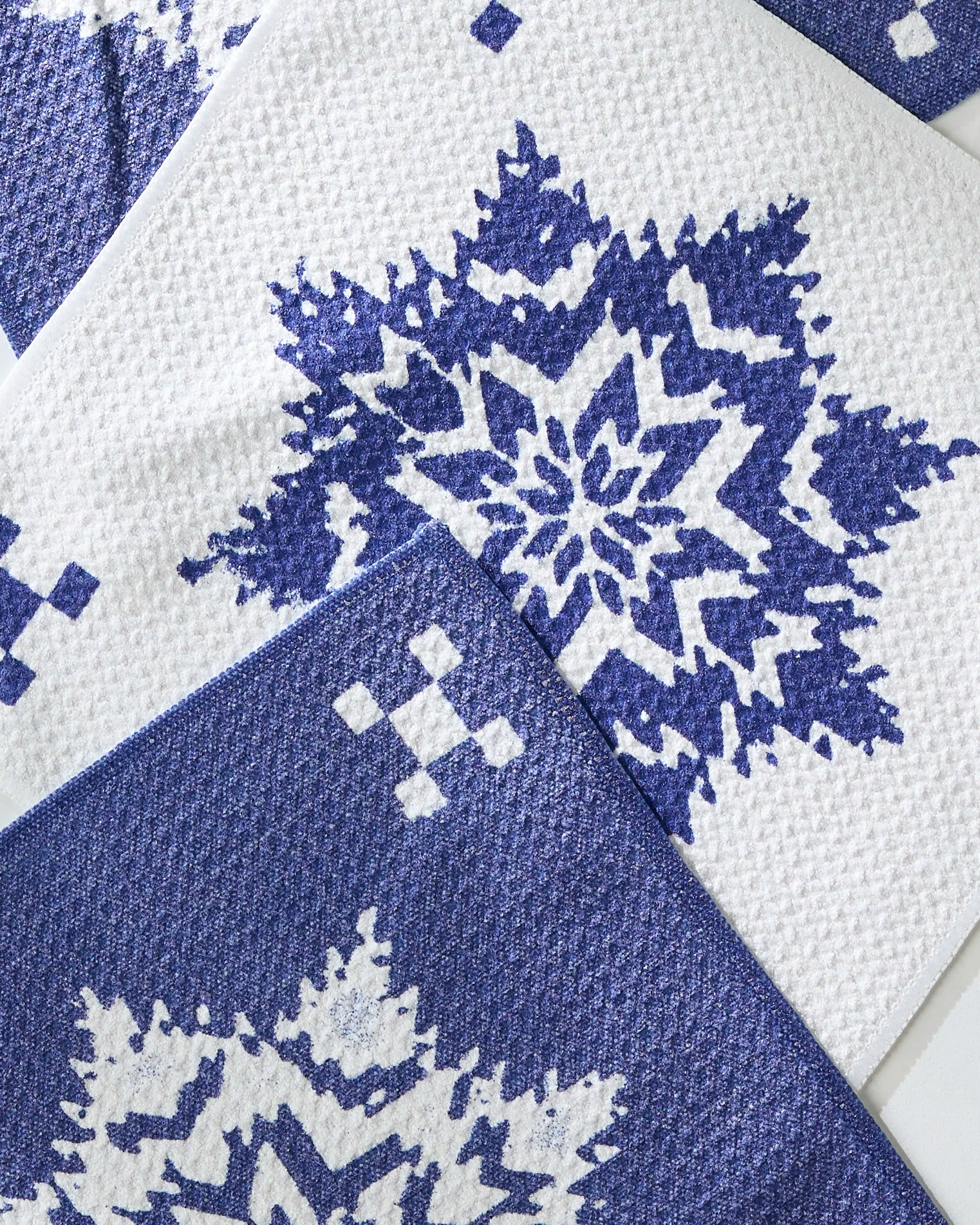 The Geometry Snowfall set features three super-absorbent dishtowels with blue and white snowflake and diamond patterns, arranged diagonally for a practical, stylish, and festive seasonal accent.