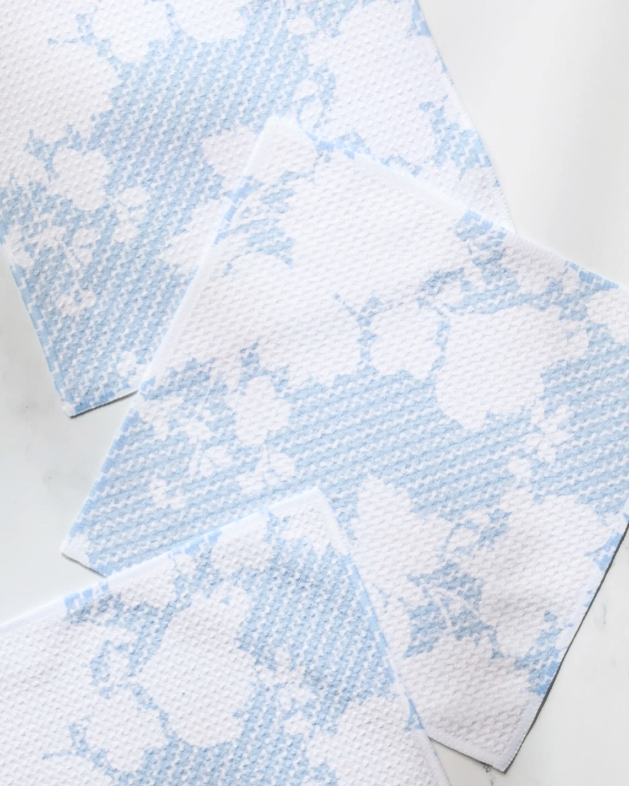 Four Geometry Soft Bloom recycled paper napkins, featuring a light blue floral and striped pattern, are arranged diagonally and partially overlapping on a white surface.
