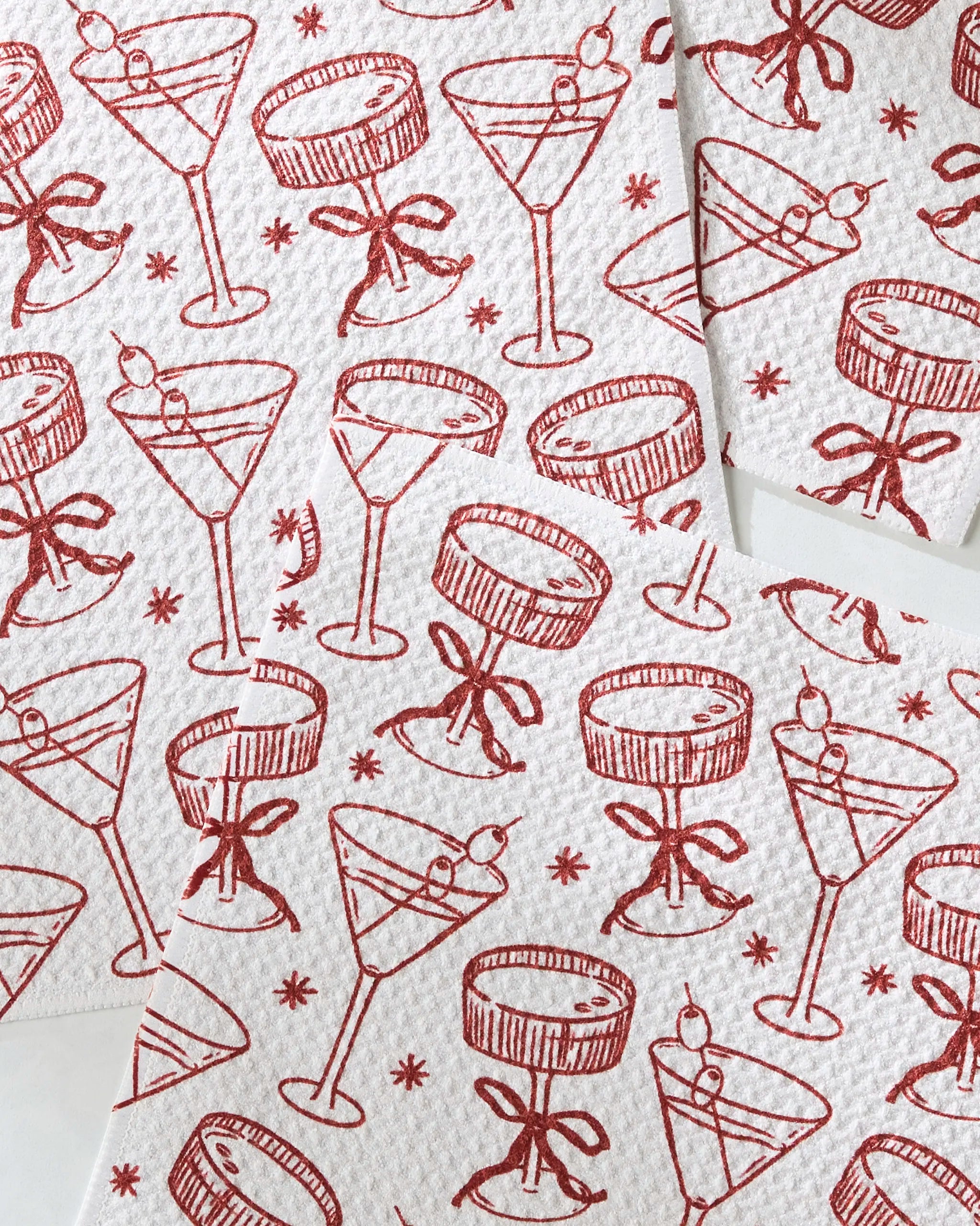 Soiree napkins by Geometry feature red line drawings of cocktail glasses—some with cherries, others with bows—on white recycled material, arranged in an overlapping pattern.