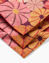 A close-up of the folded Spicy Pumpkins rug by Rebecca Bobko displays large, stylized flowers in pink, orange, yellow, and purple hues with textured details—evoking vibrant recycled dishcloth designs.