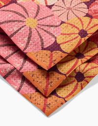 A close-up of the folded Spicy Pumpkins rug by Rebecca Bobko displays large, stylized flowers in pink, orange, yellow, and purple hues with textured details—evoking vibrant recycled dishcloth designs.