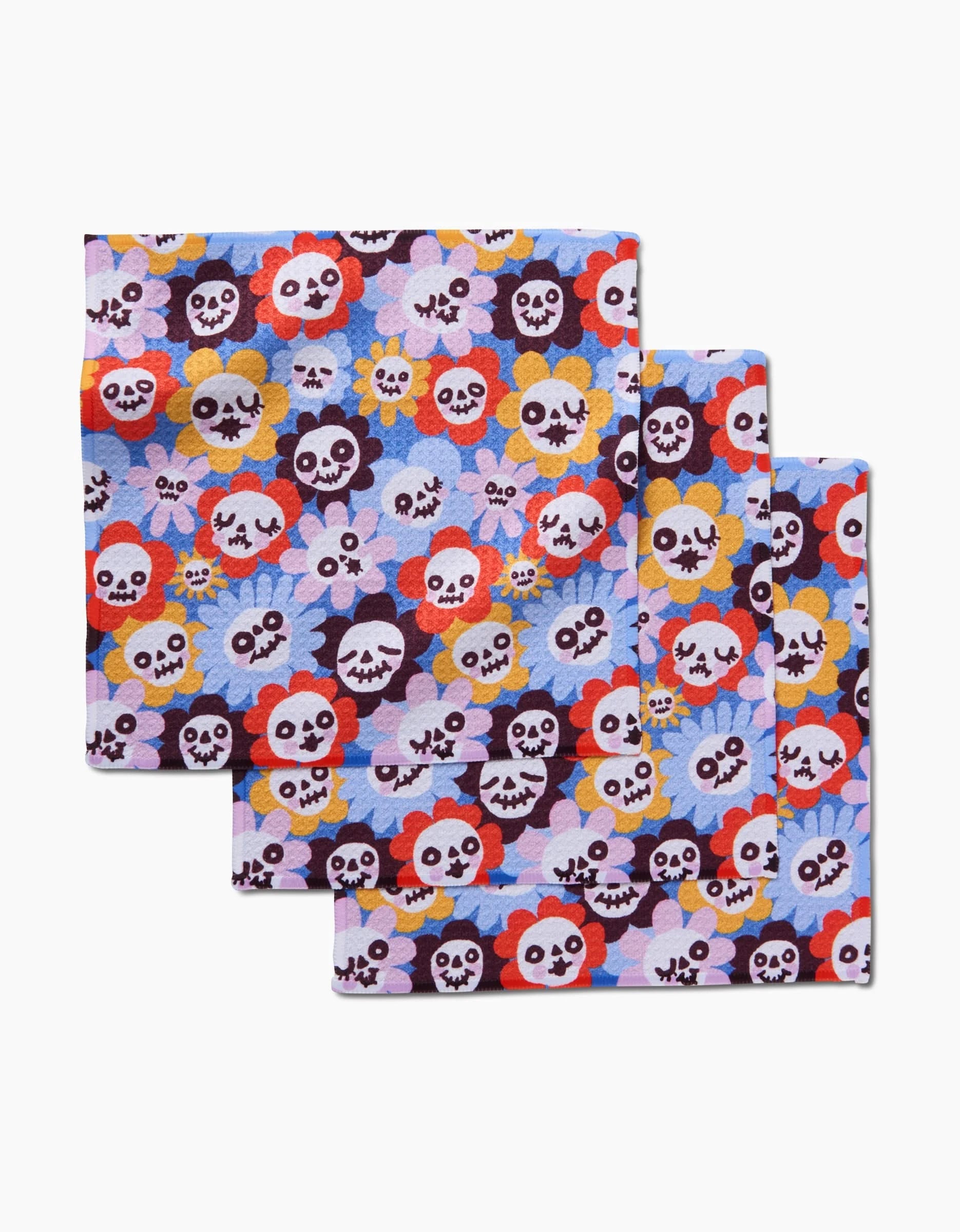 The Spooky Bouquet dishcloth set by So Lazo features three folded cloths with cartoon skulls, flowers, and butterflies in bright colors on light blue—fun and eco-friendly, made from recycled materials.