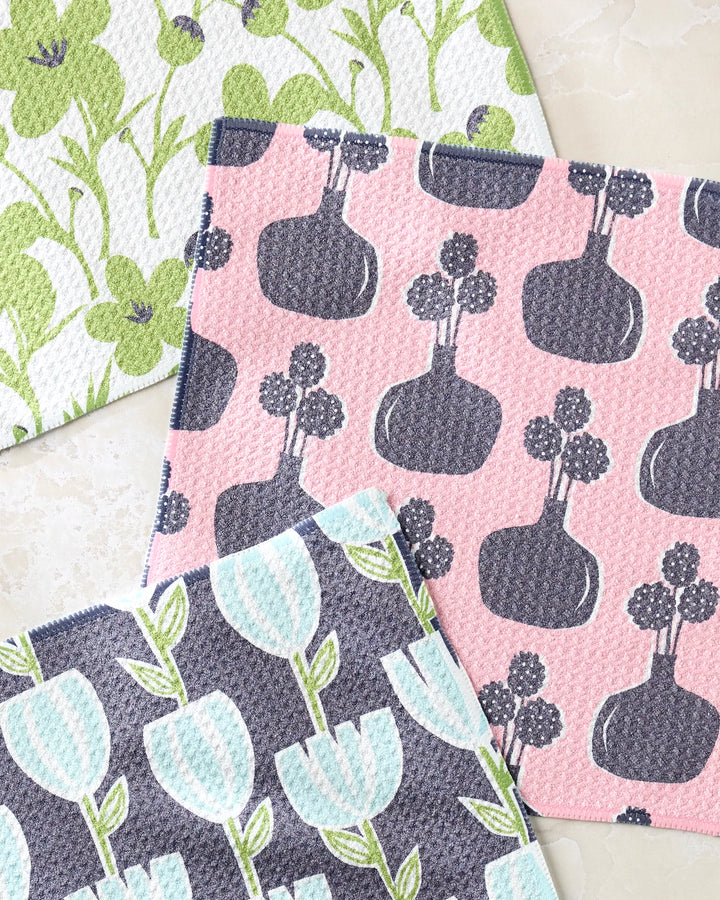Lizzie Clark’s Spring Bouquet set features three patterned dishcloths: one with green flowers, one with blue tulips and green stems, and one with gray vases and round flowers on a pink background. All are made from recycled materials.