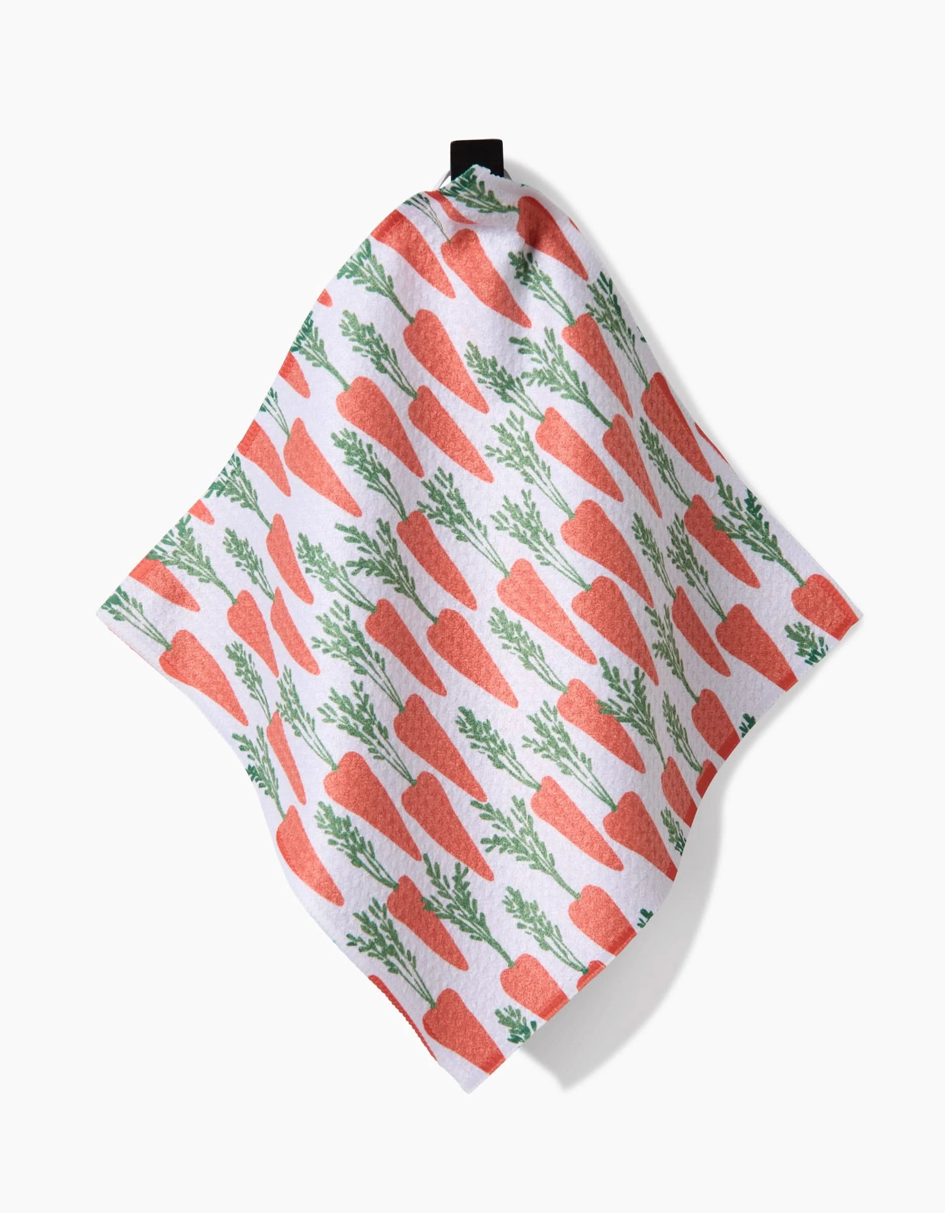 The Spring Carrot Hill dishtowel by Hufton Studio is super-absorbent and white, featuring a repeating pattern of orange carrots with green tops, and hangs by a black loop against a plain white background.
