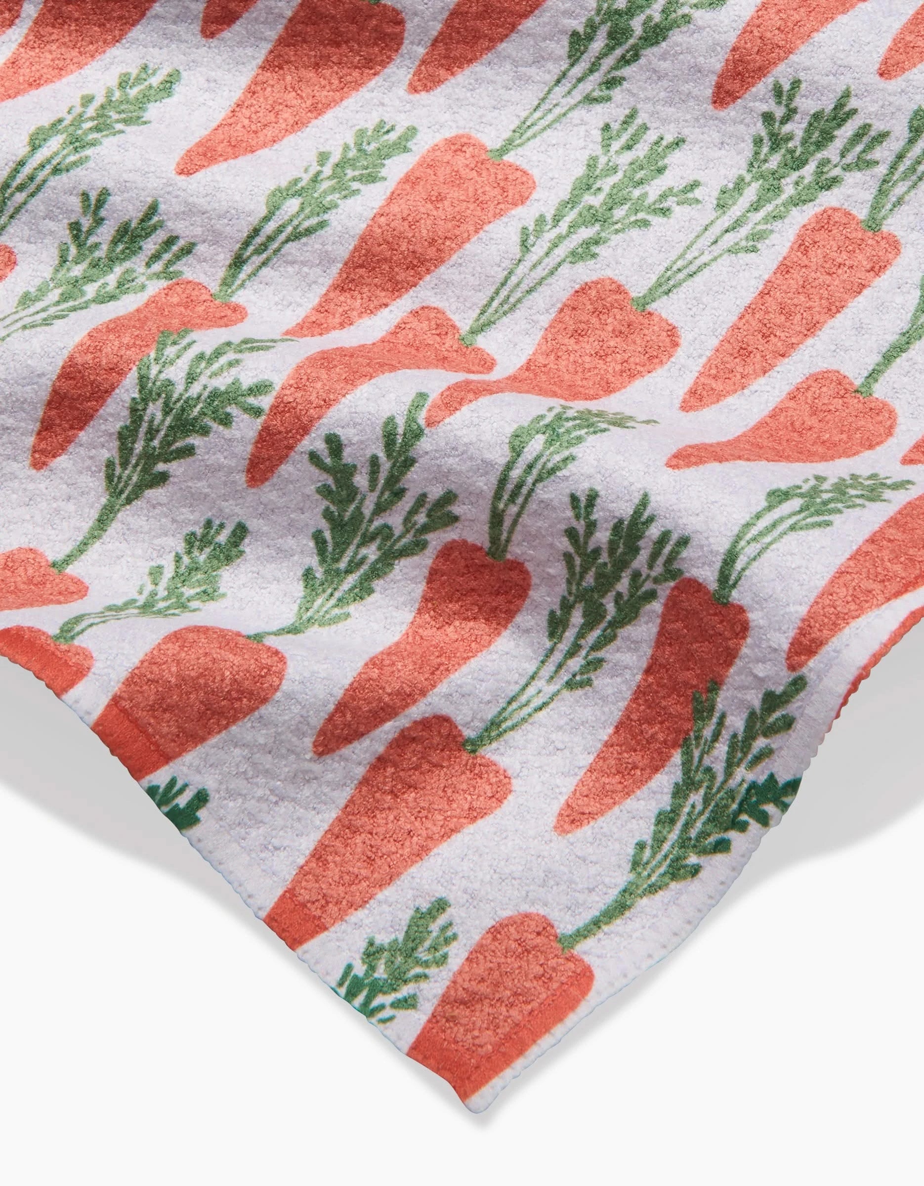 The Spring Carrot Hill towel by Hufton Studio is a white recycled-fabric towel with rows of orange carrots and green tops, shown at an angle with part of the edge visible.