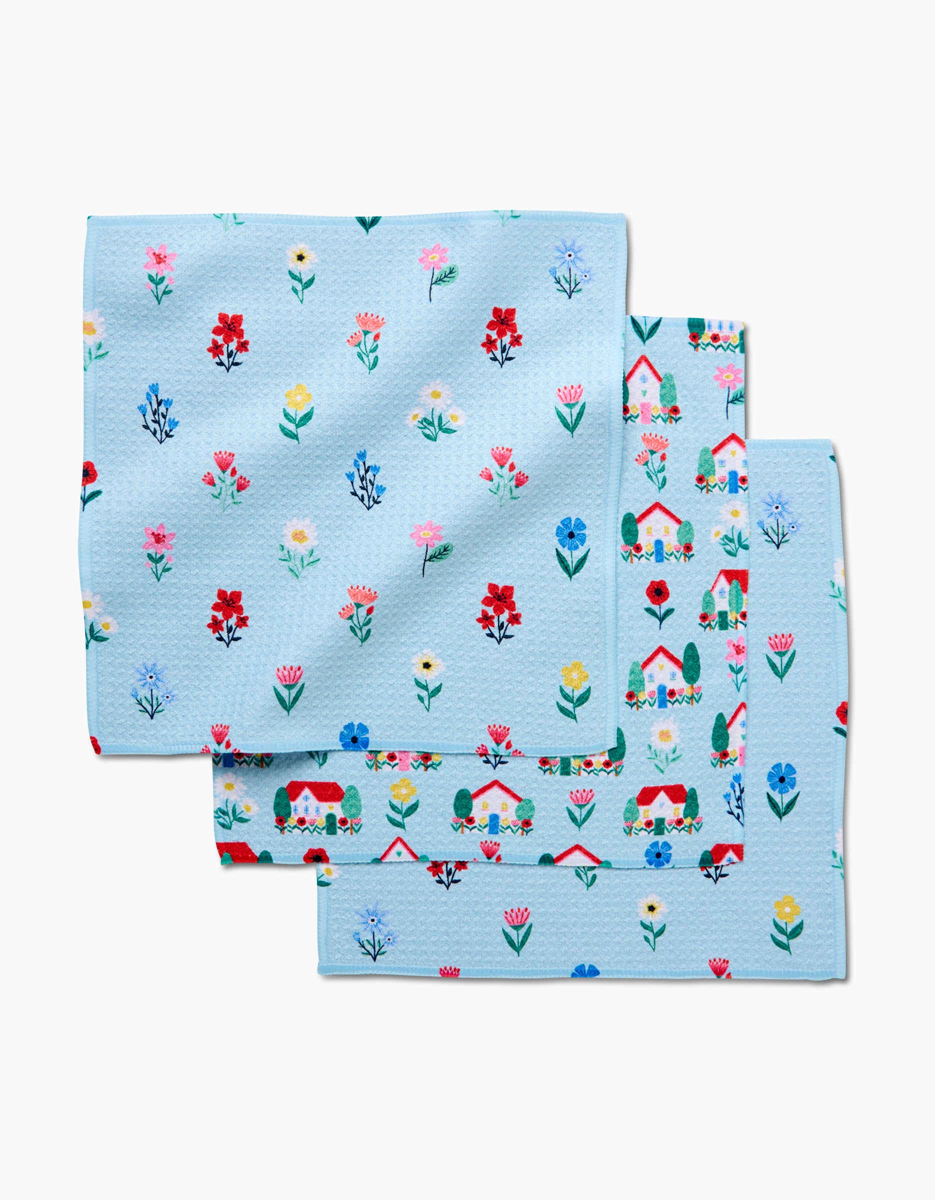 Three light blue Spring House Blossom Geoweave napkins by Ceyda Alasar, featuring a vibrant red, yellow, white, and blue floral pattern, are neatly stacked with overlapping corners for a lively dishcloth set.