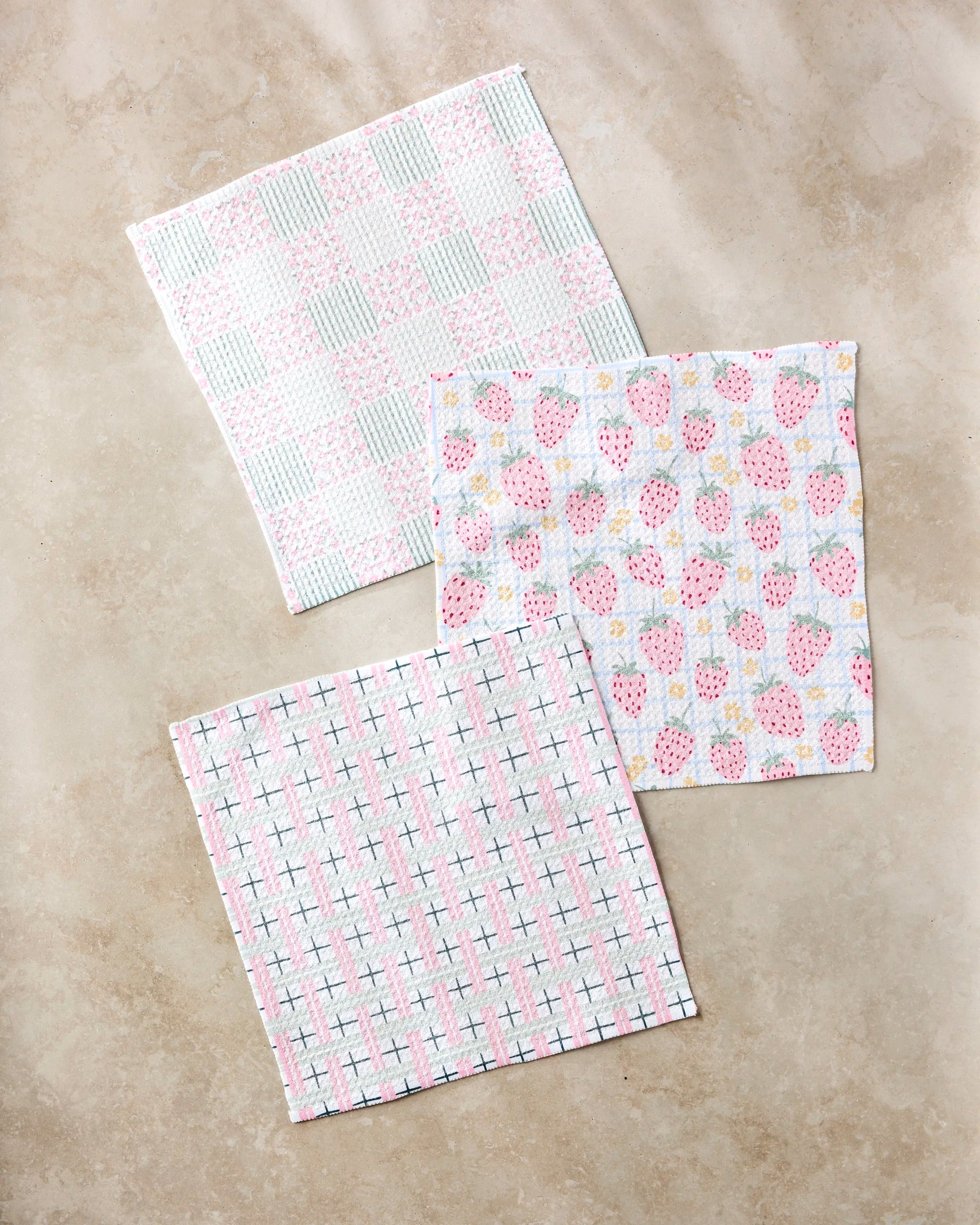The "Spring Picnic Day" set by Hufton Studio includes three recycled cloth napkins in pastel checkered, strawberry, and cross patterns, displayed on a light beige marble surface.