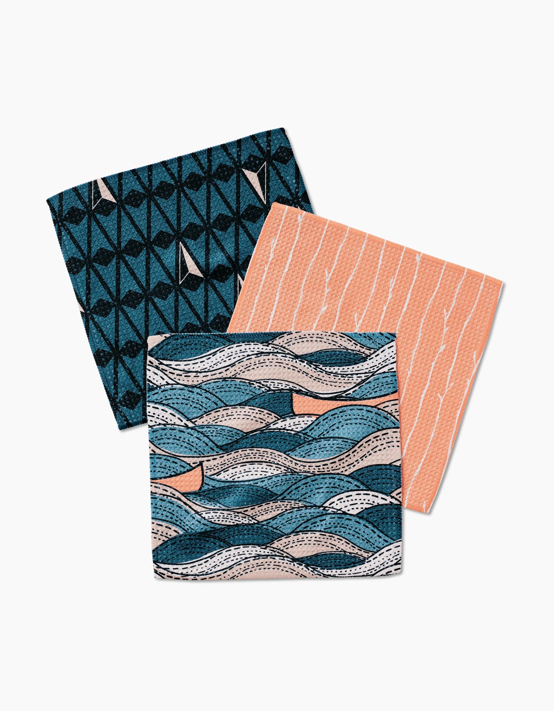 Three Squall napkins by Twig + Spark, made from Geoweave fabric with blue, peach, and black geometric and wave patterns, are arranged overlapping on a white background.