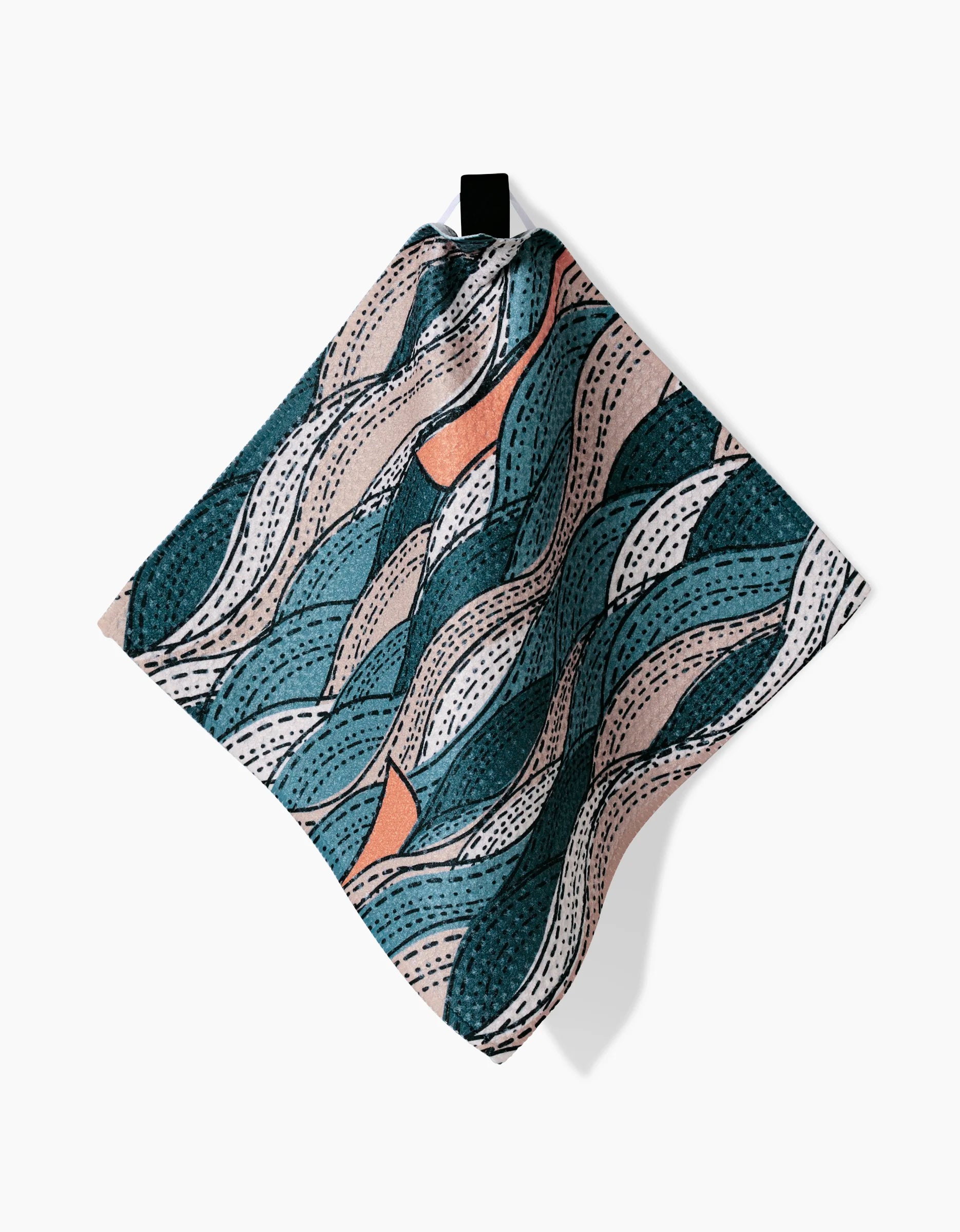 The Twig + Spark Squall dishcloth, made from Geoweave fabric, displays wavy teal, peach, and beige shapes with dotted lines, and hangs from a black loop against a white background.