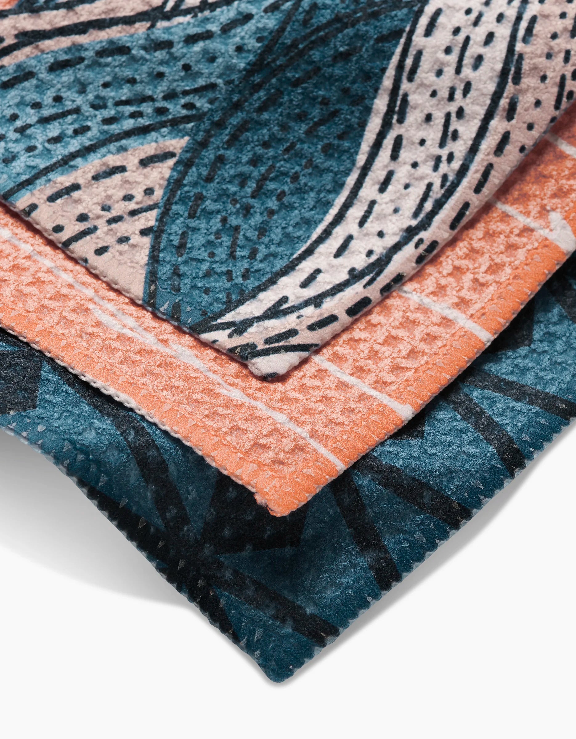 Close-up of two Squall Geoweave fabric pieces by Twig + Spark, one teal/black and one orange/white, layered to showcase their detailed texture and stitching—ideal for stylish, durable dishcloths.