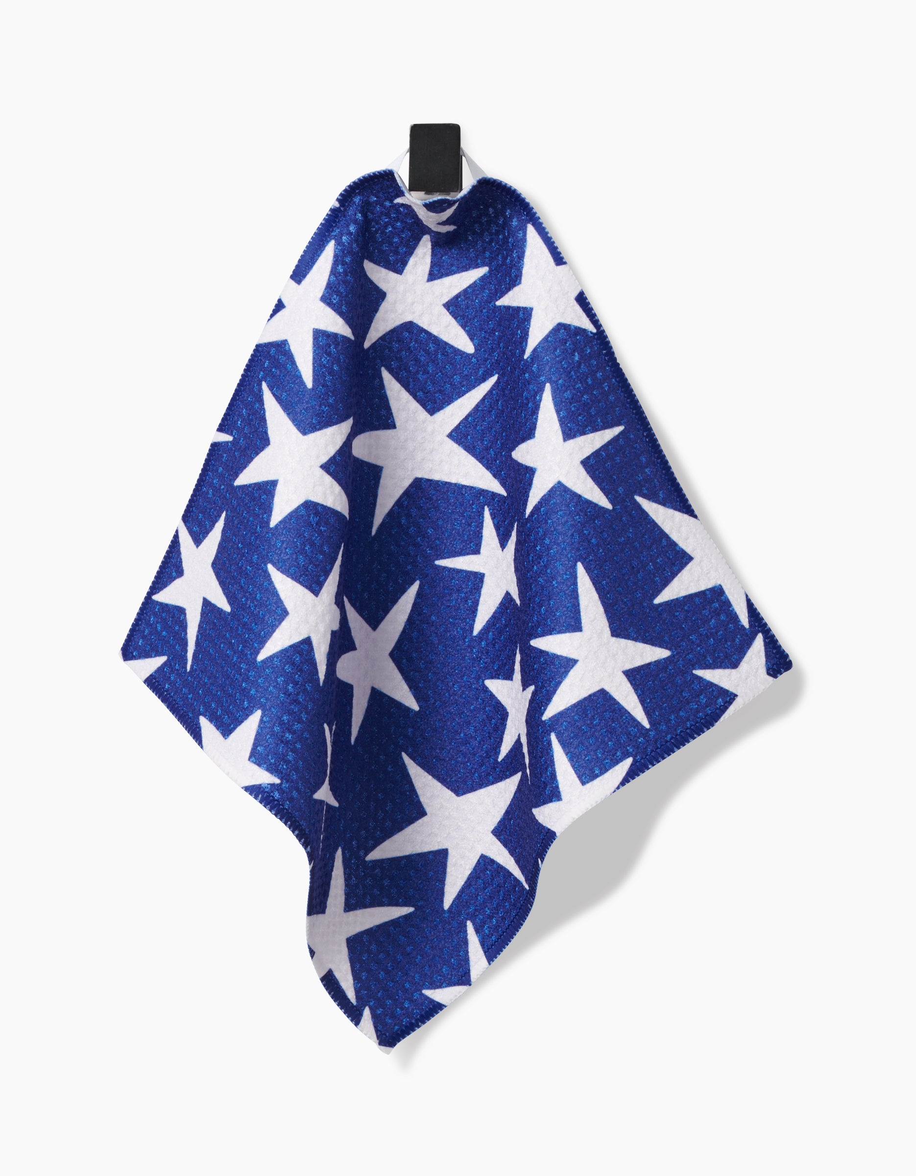 The Mindfulnice Stars And Stripes towel, crafted from super-absorbent recycled materials and decorated with blue and white stars, hangs from a black hook against a white background.