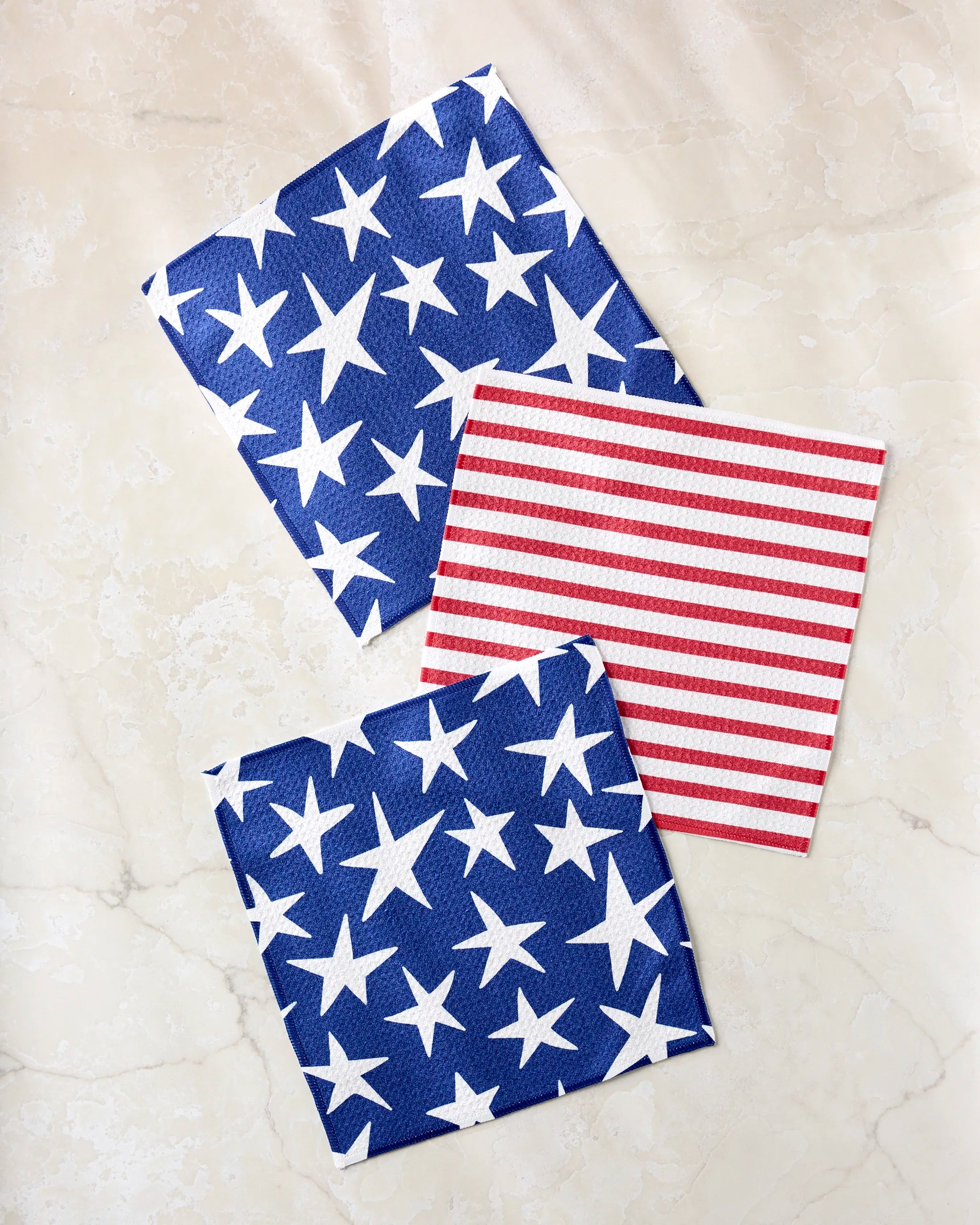 Mindfulnice’s Stars And Stripes set: three eco-friendly napkins—two blue with white stars, one red-and-white striped—evoke the American flag and are made from recycled materials.
