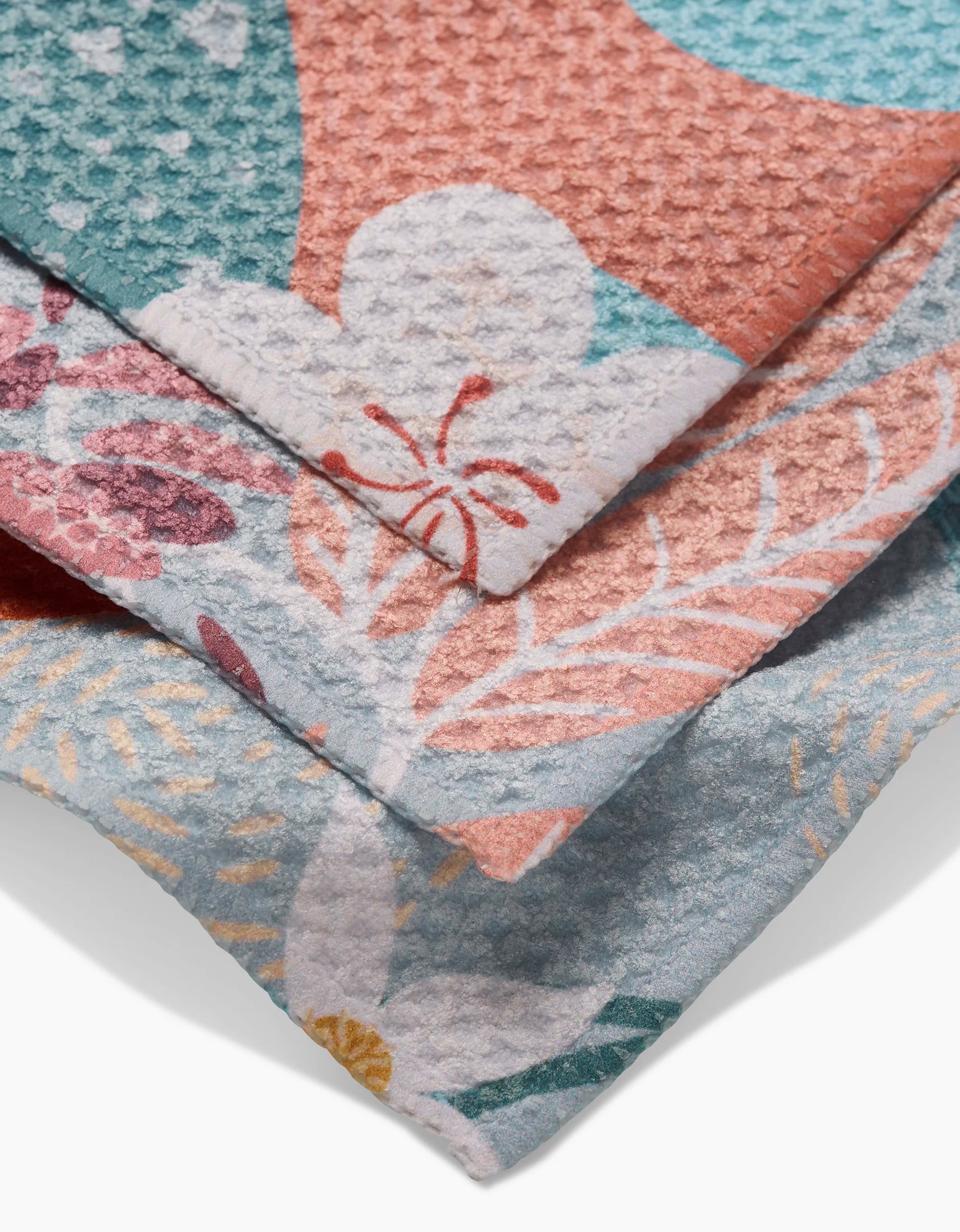 A close-up of three Julianne Haness State Flowers dishcloths layered together, showing pastel teal, coral, pink, and white floral patterns on super-absorbent Geoweave fabric.