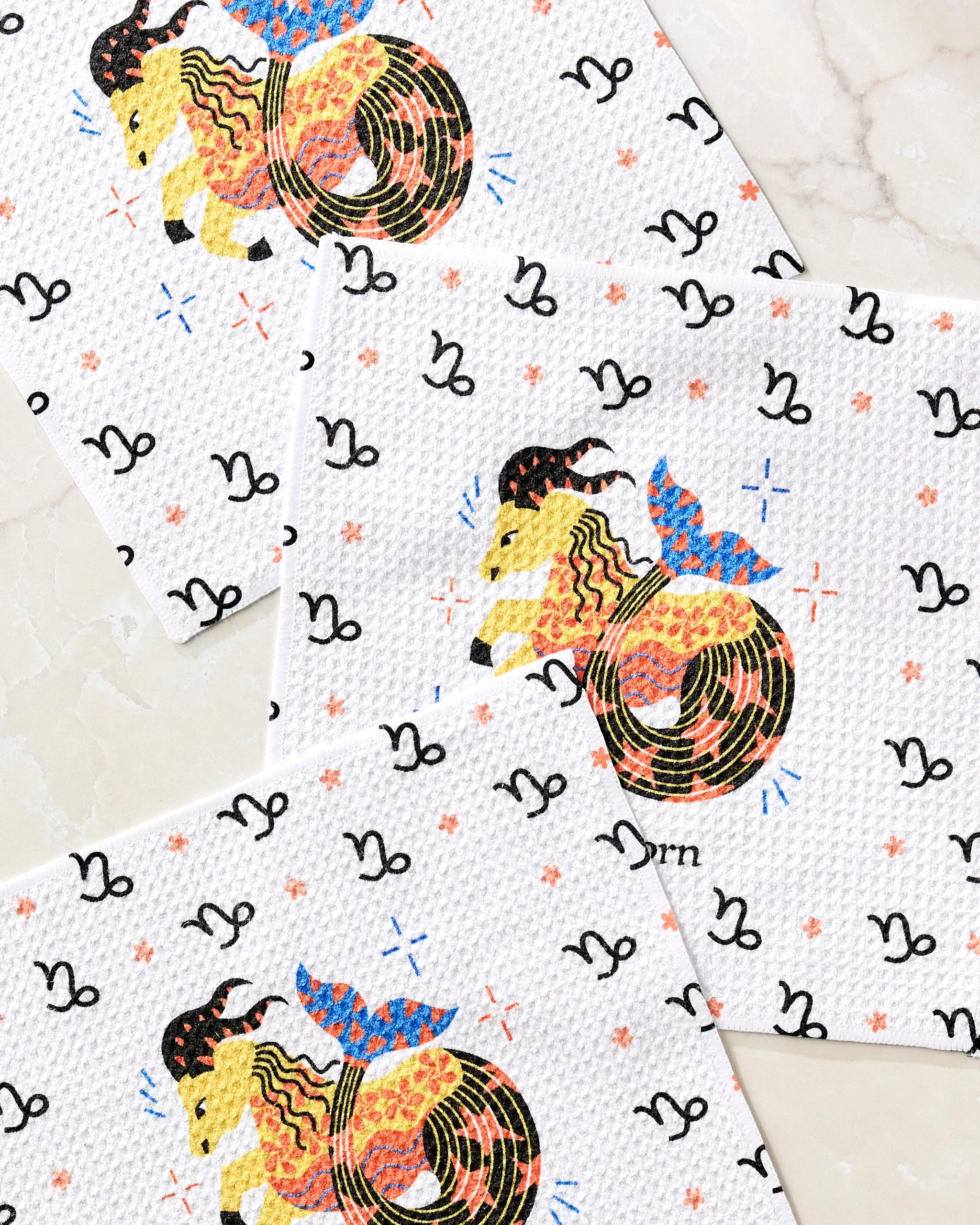 The Steadfast Capricorn dishcloth set by Heather Zhou includes three recycled towels with Capricorn goat-fish symbols, colorful stars, and black zodiac motifs—perfect for any zodiac fan's kitchen.
